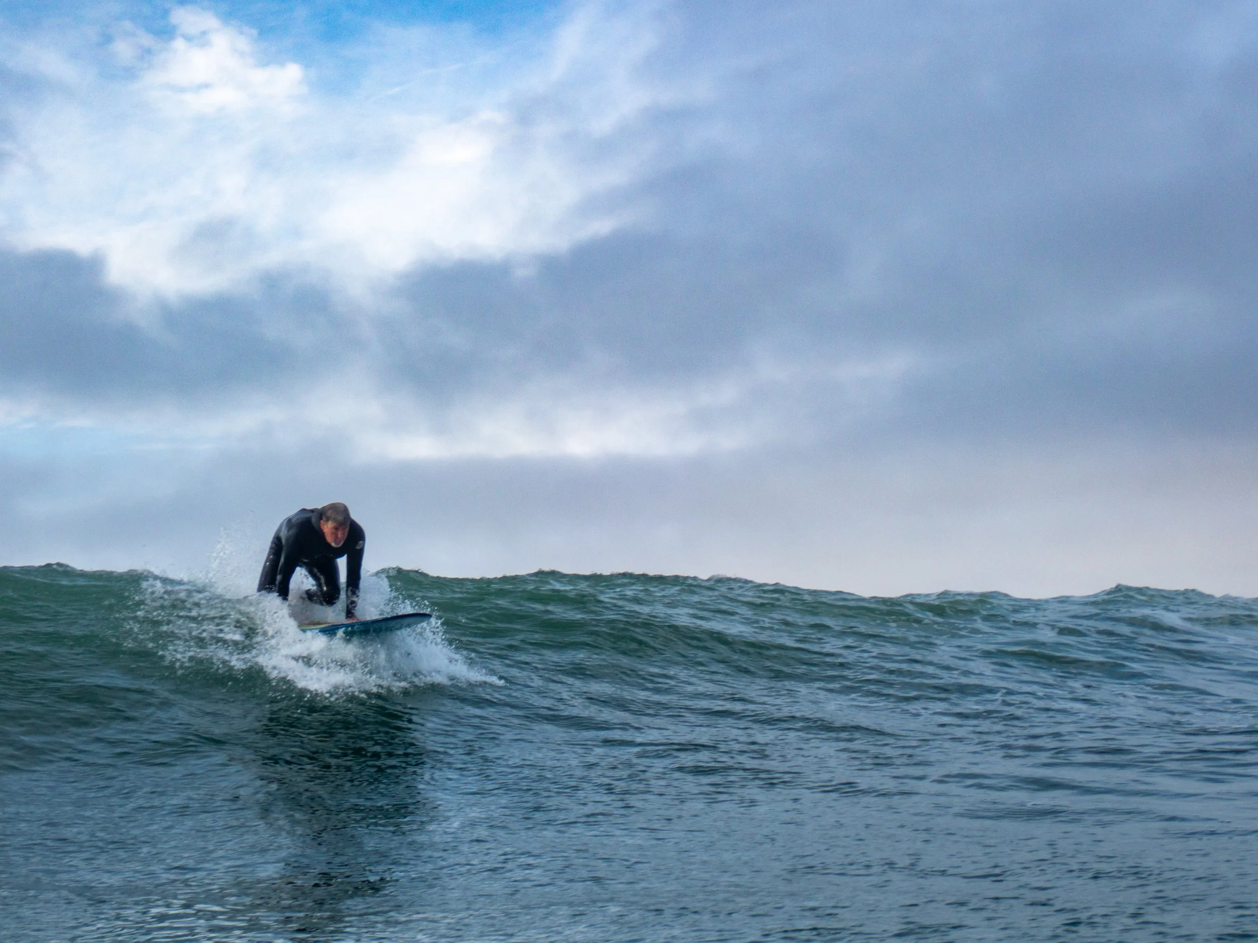 A person in a wetsuit surfing on a wave in the ocean under a cloudy sky.