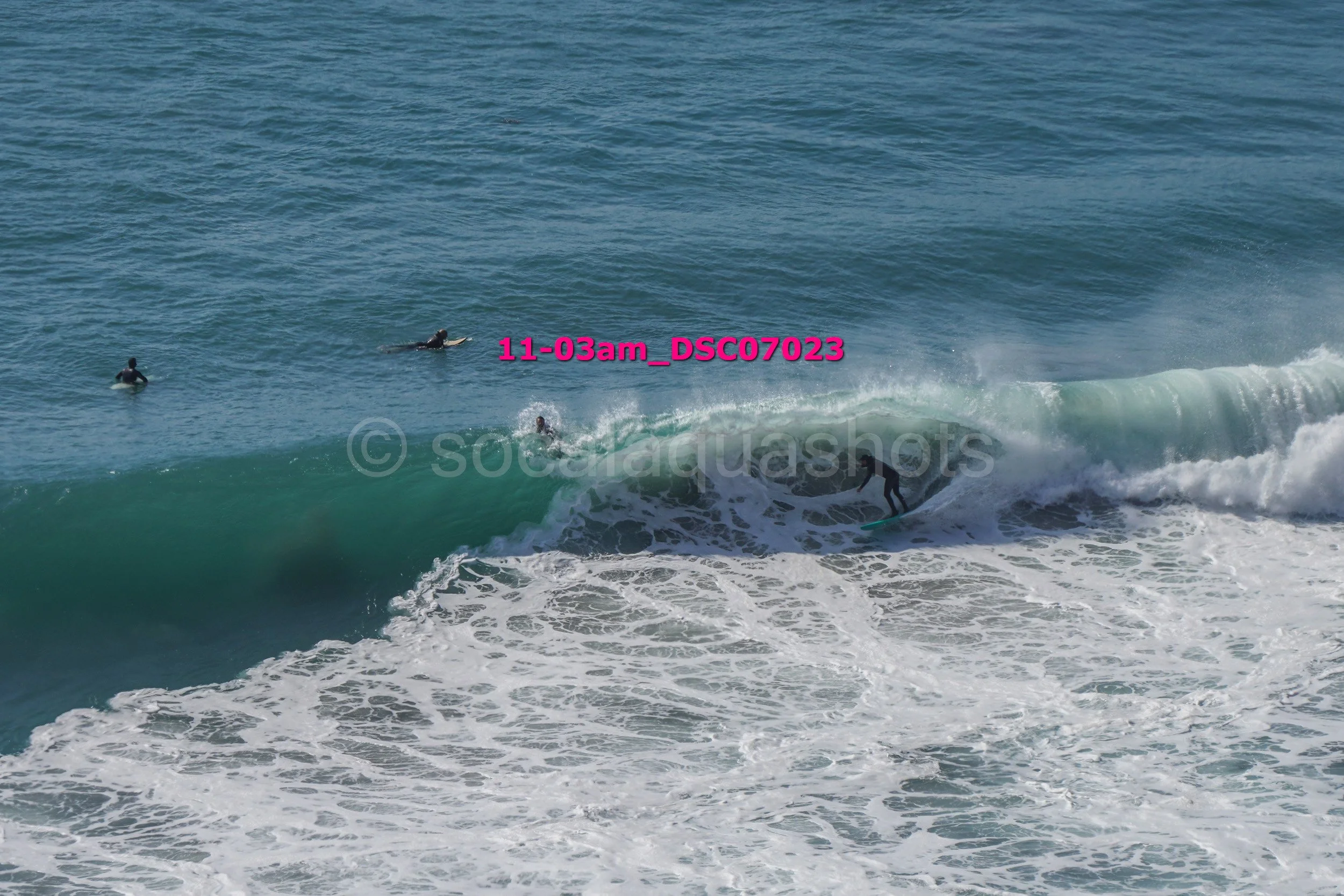 Surfers in the ocean riding and waiting for waves amidst blue waters and foamy white waves.