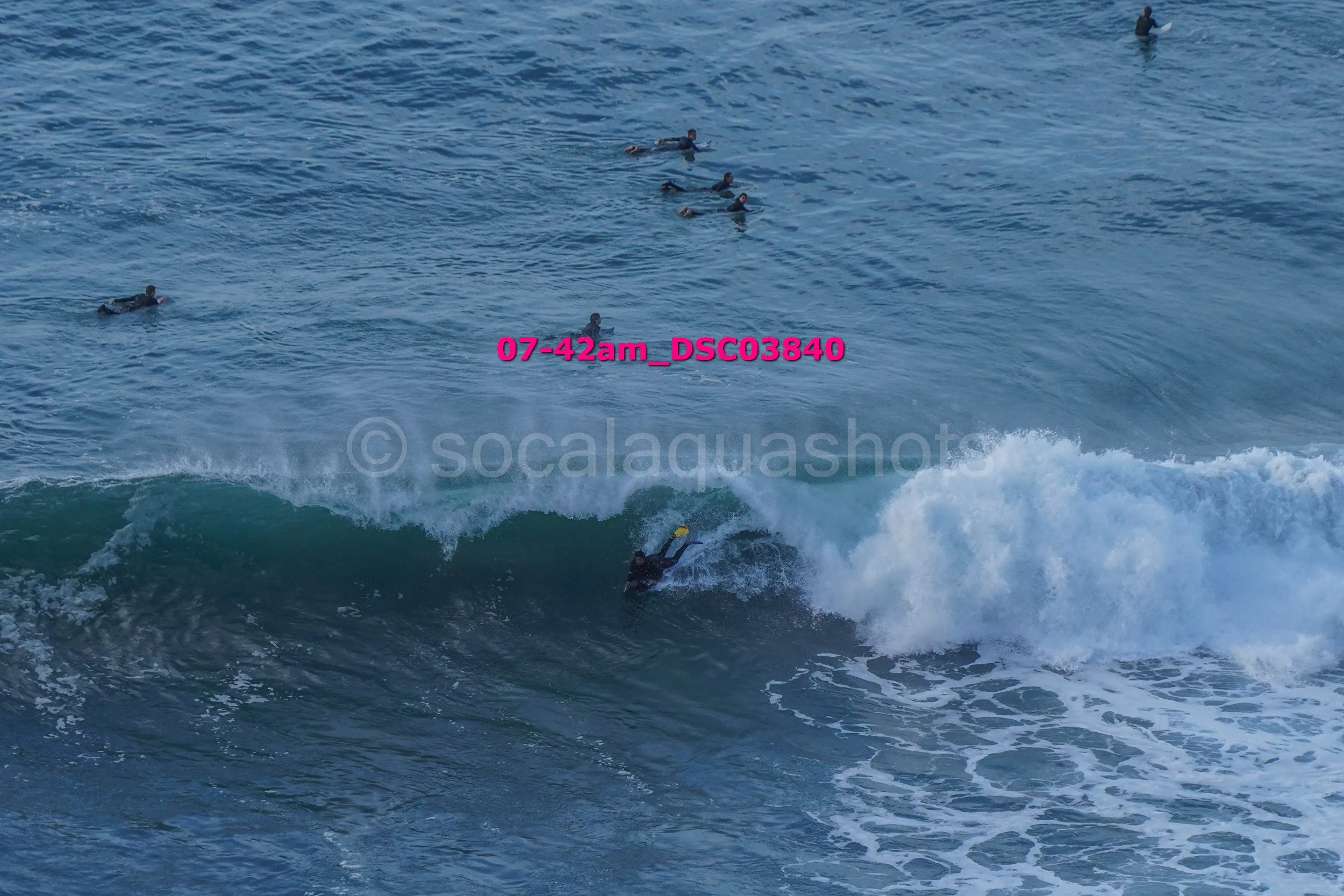 A surfer riding a wave with several surfers in the water in the background.
