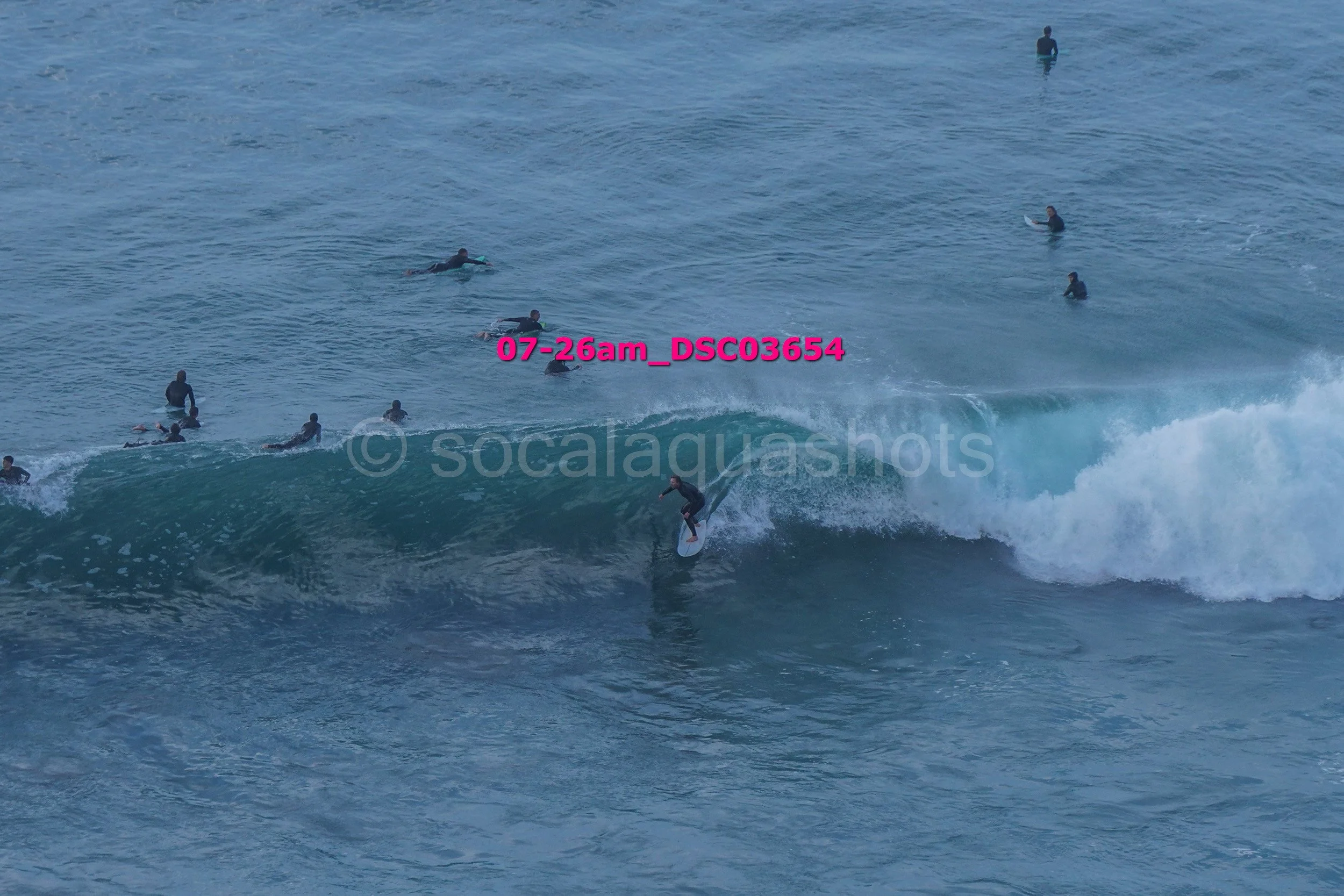 Surfer riding a wave in the ocean with multiple surfers in the water in the background.