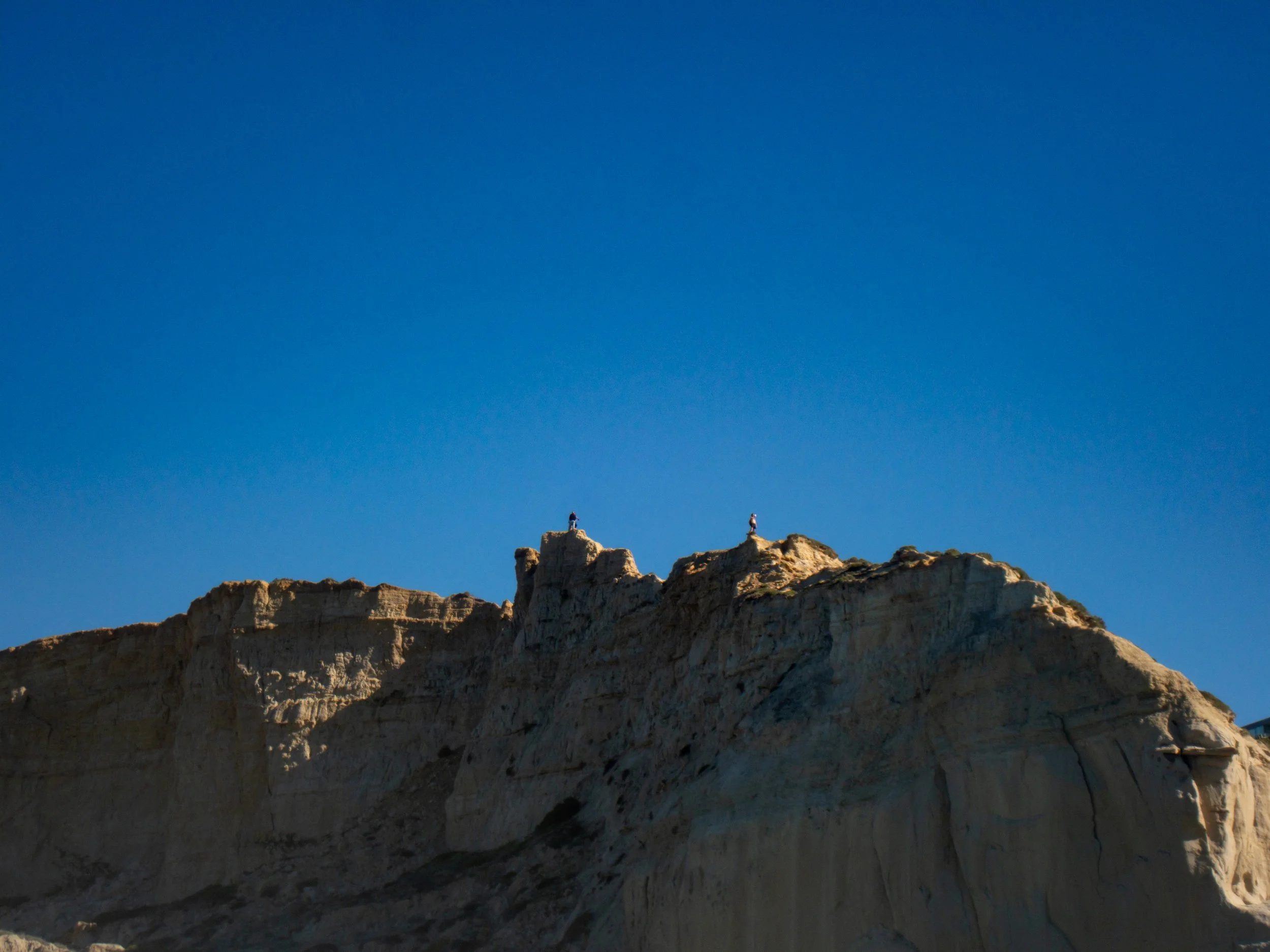 Cliffs with a clear blue sky, two people standing at the top of the cliffs.