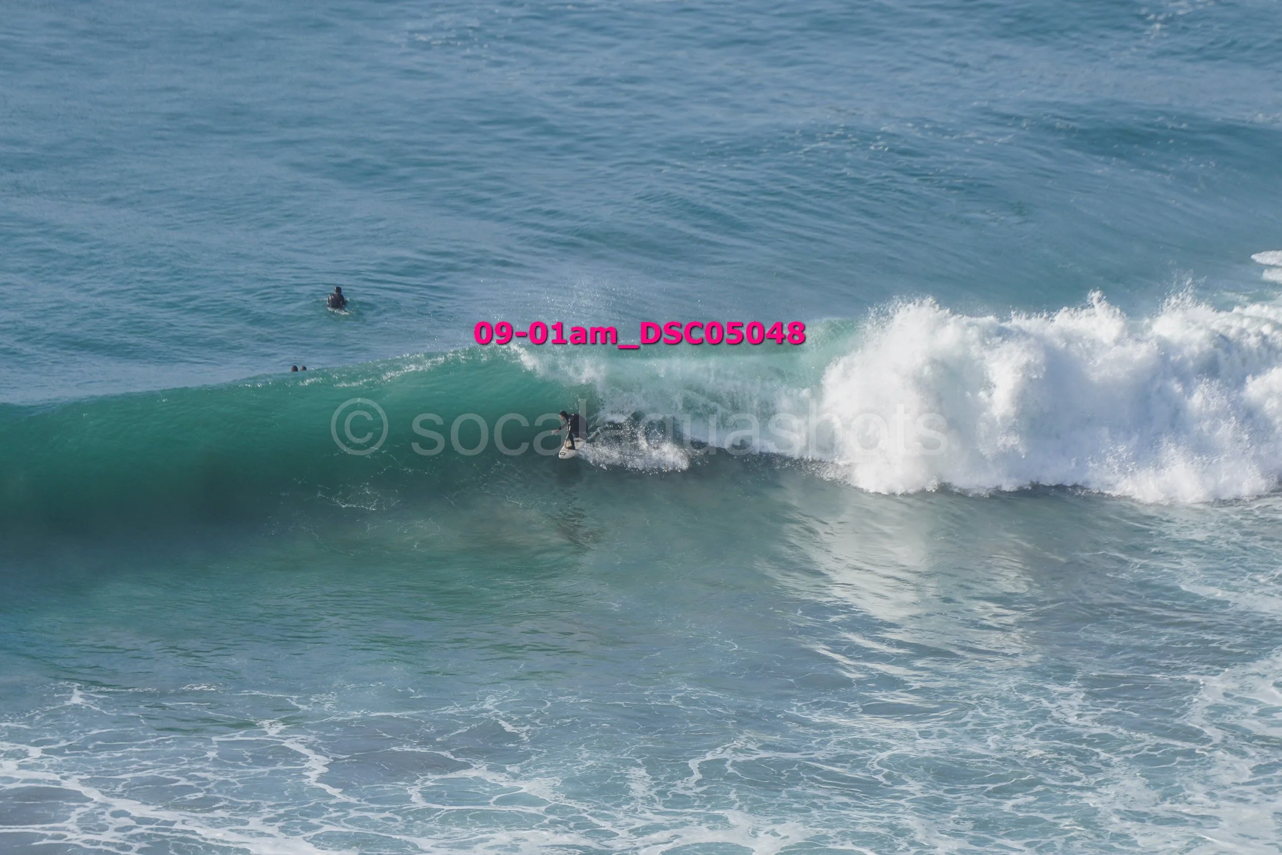 Surfer riding a wave in the ocean with three other surfers in the distance.