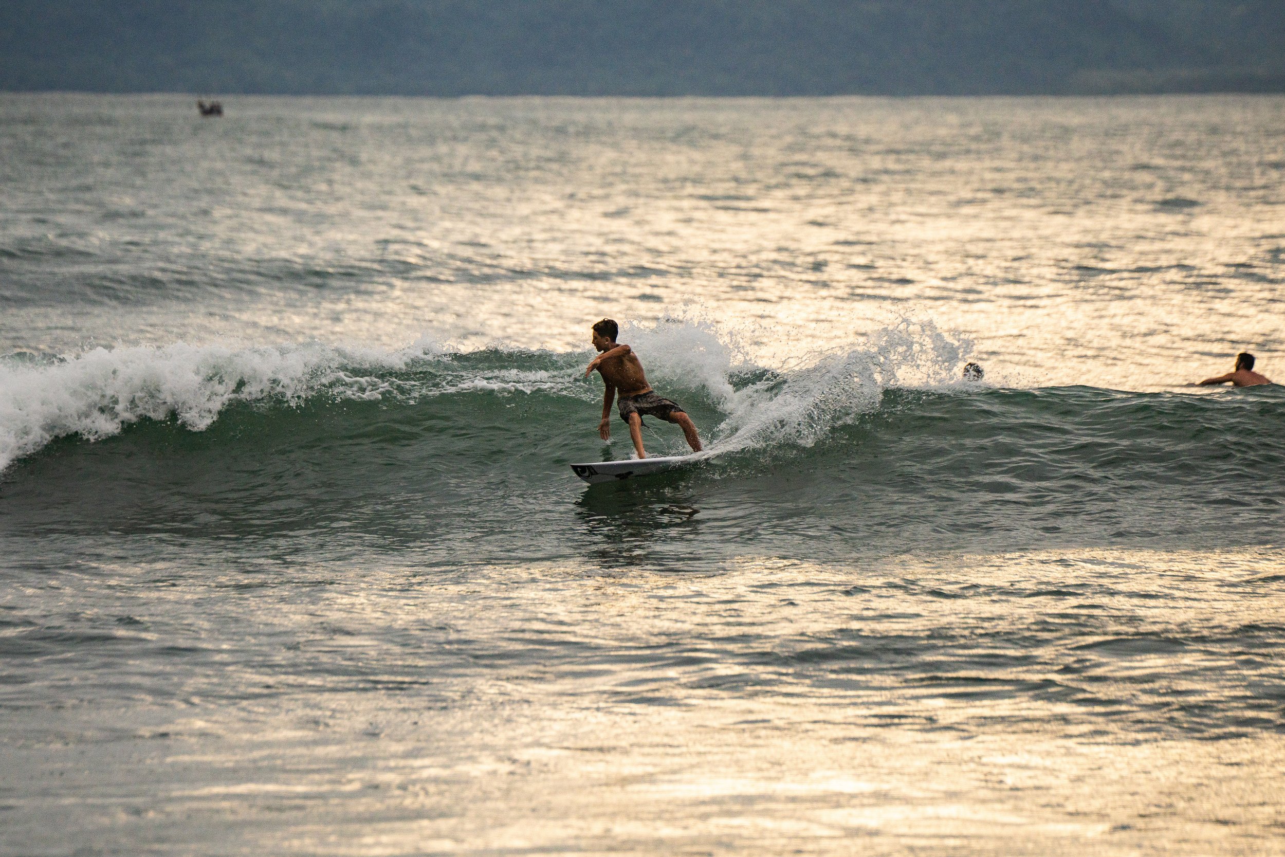 A person surfing on a wave in the ocean during sunset or sunrise with other surfers in the background.