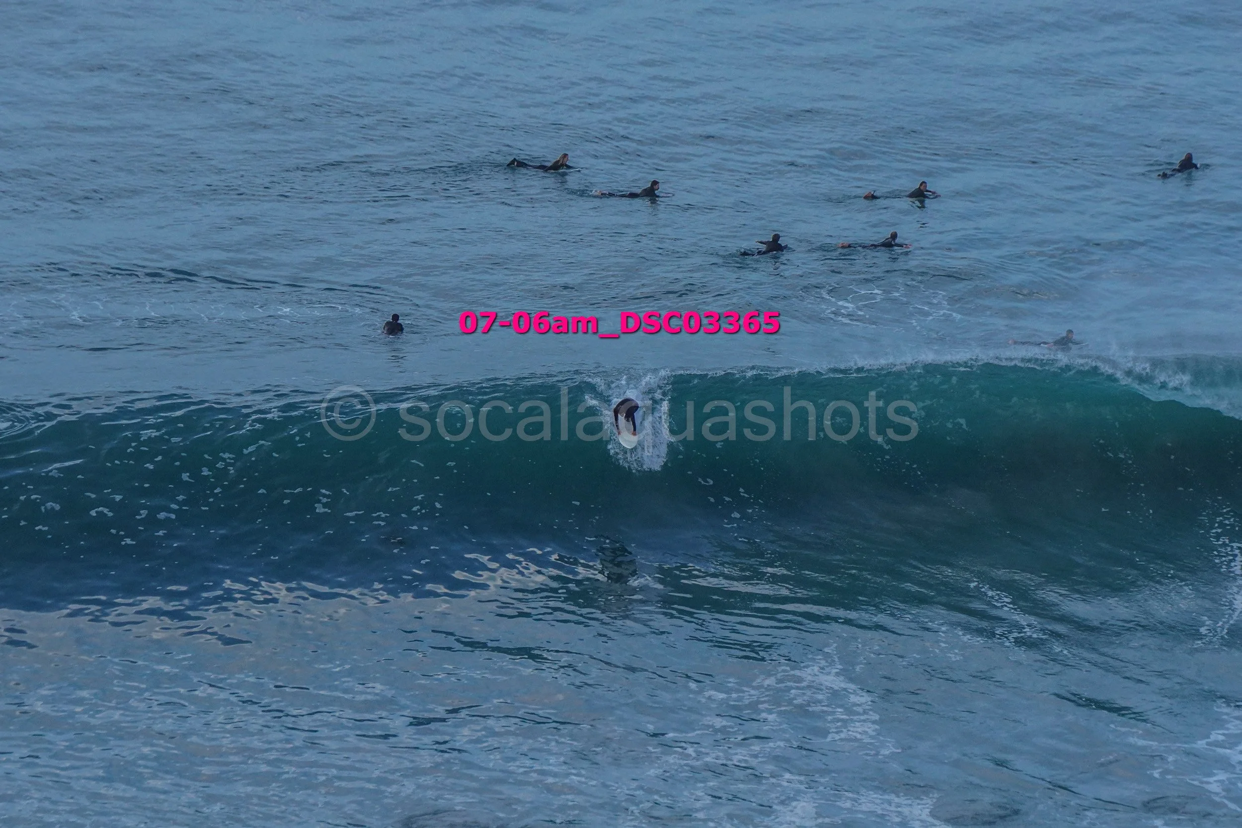 A person surfing on a wave while several other surfers are in the water in the background.