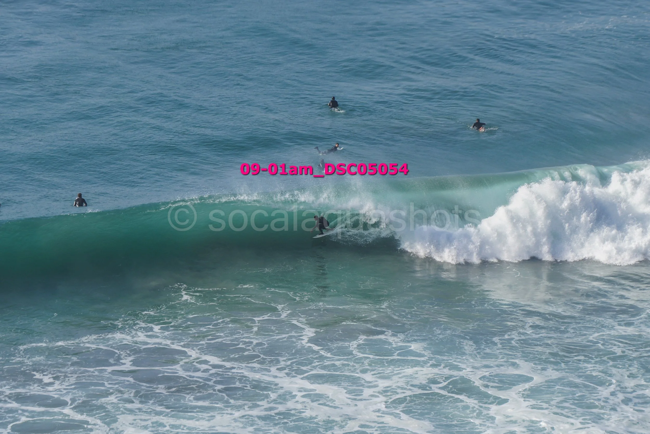 Surfer riding a wave with other surfers in the background in the ocean.