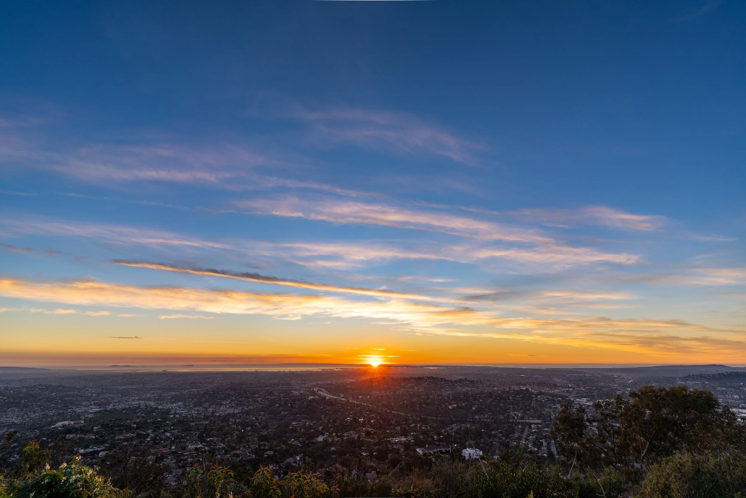 Sunset over a cityscape with a colorful sky and scattered clouds.