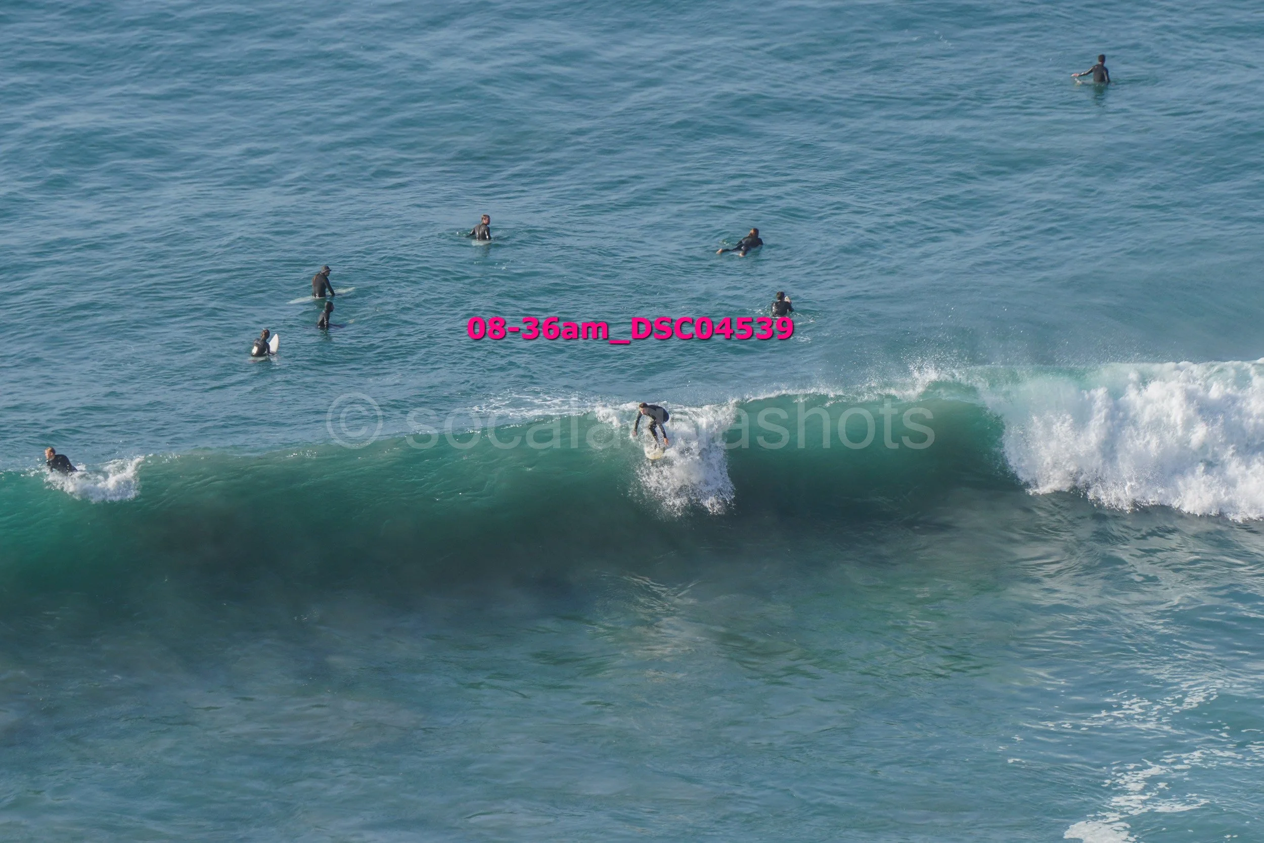 Surfer riding a wave with several people in the water watching nearby