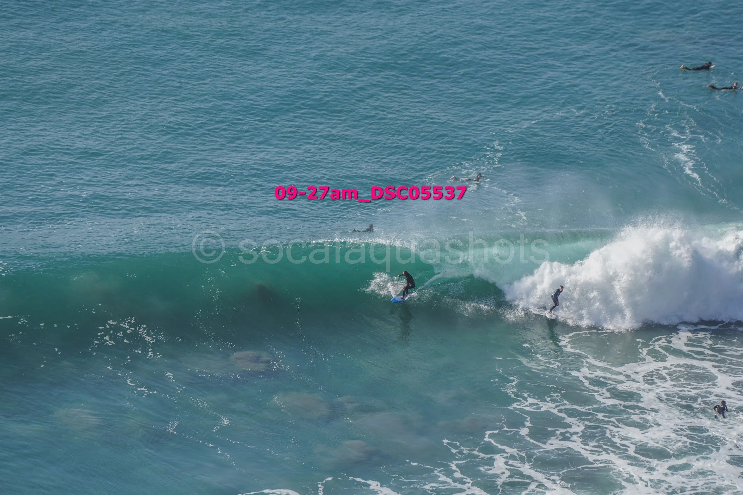 A group of surfers riding a large wave in the ocean, with some surfers paddling in the water nearby.