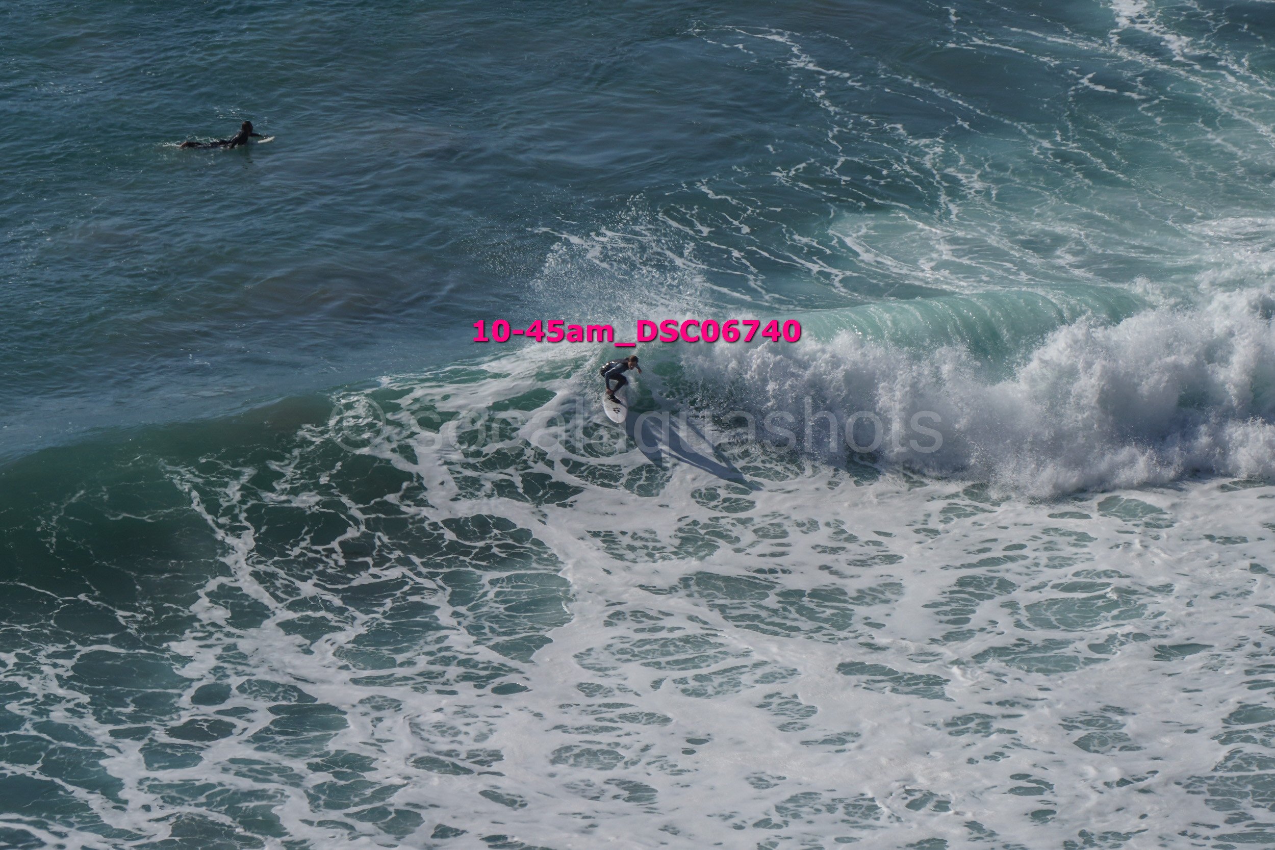 A person surfing on a large wave with another person in the water nearby.