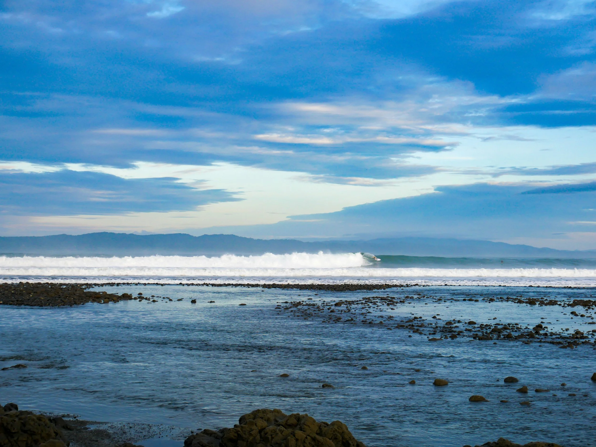 Scenic coastal view with ocean waves, cloudy sky, and distant land silhouette.