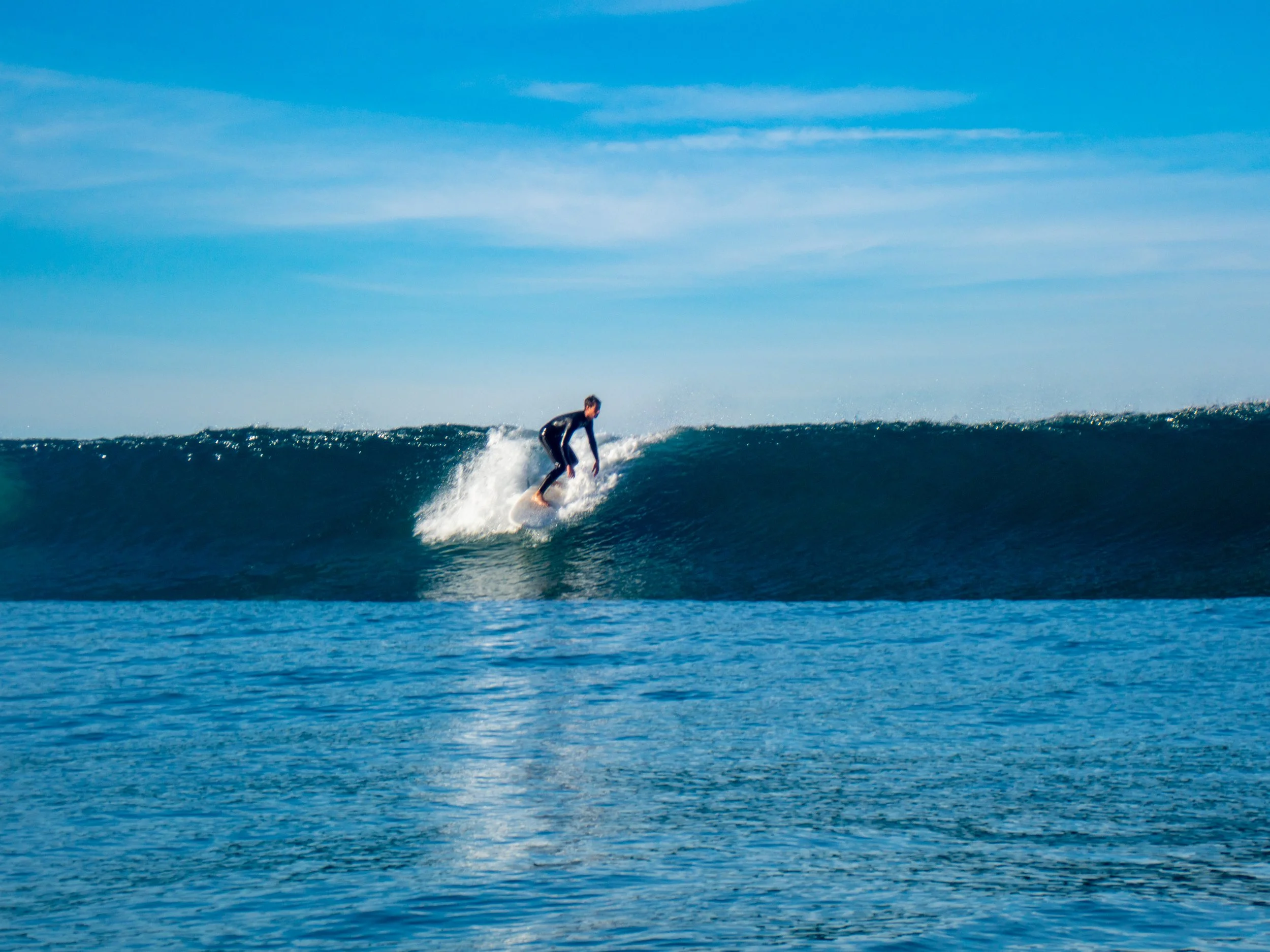 A person surfing on a wave in the ocean under a clear blue sky.
