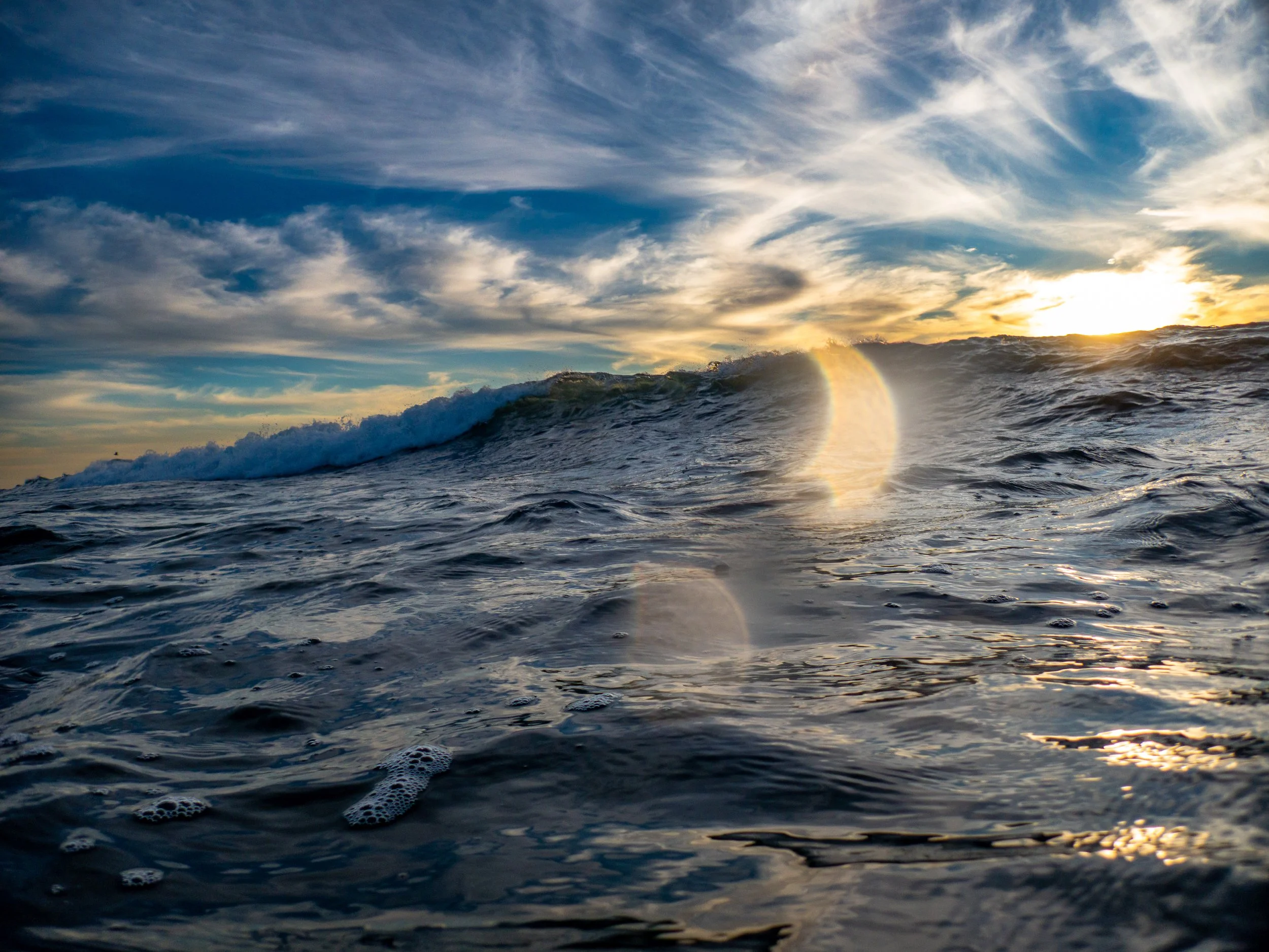 Sunset over the ocean with waves and clouds in the sky, sunlight reflecting on the water.