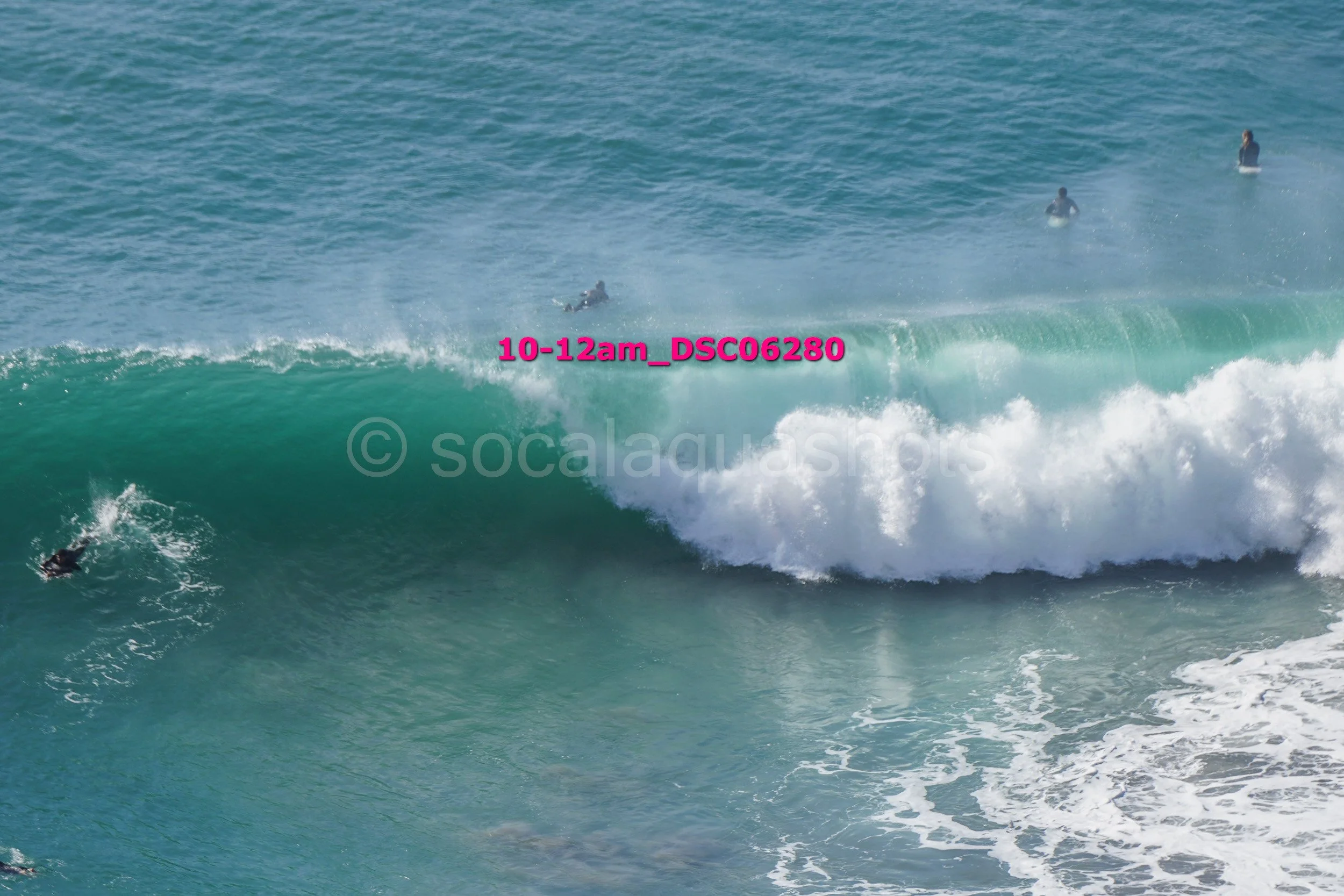 Multiple surfers in the ocean, with some riding a wave and others waiting in the water.