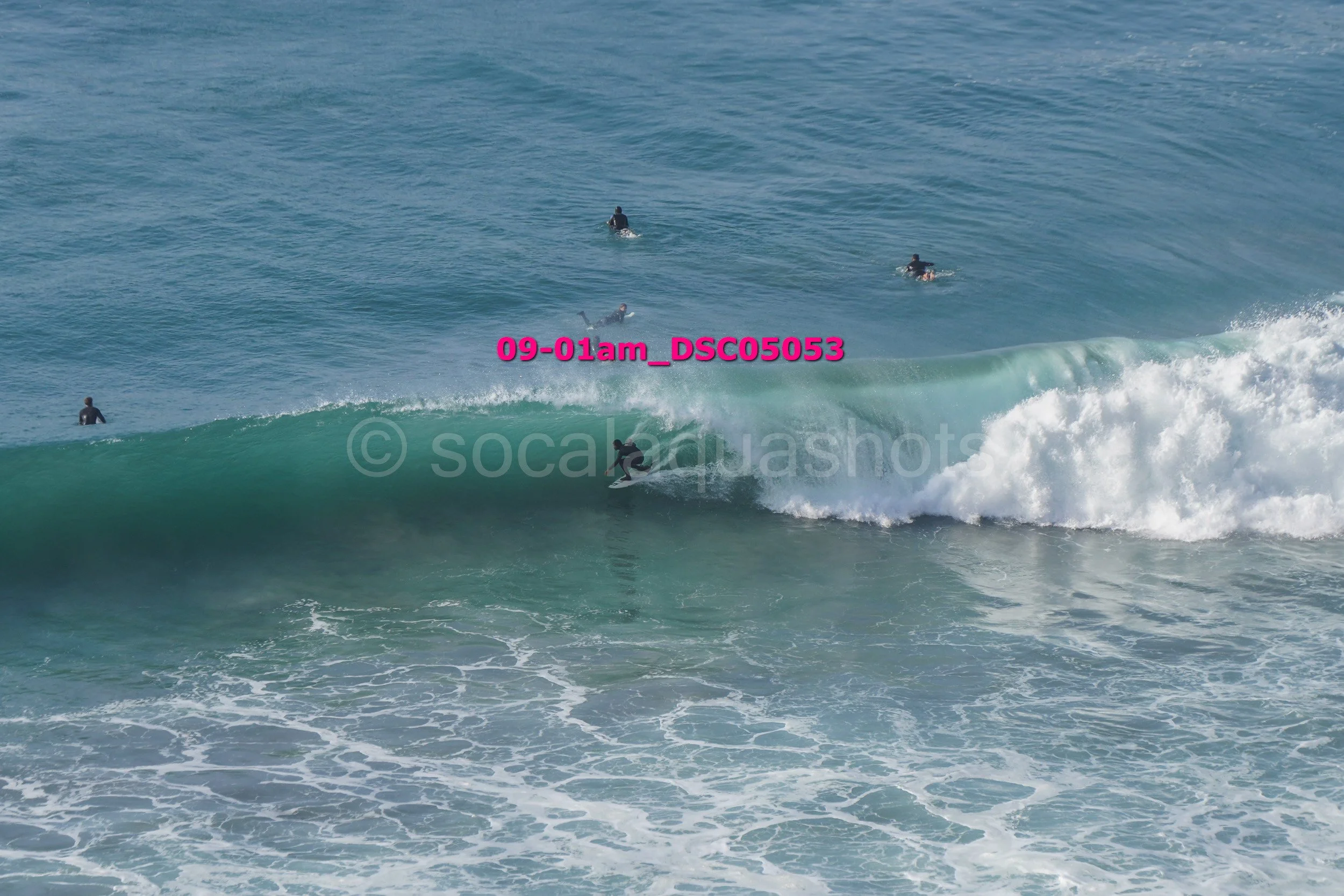 A surfer riding a wave with five other surfers in the water nearby.