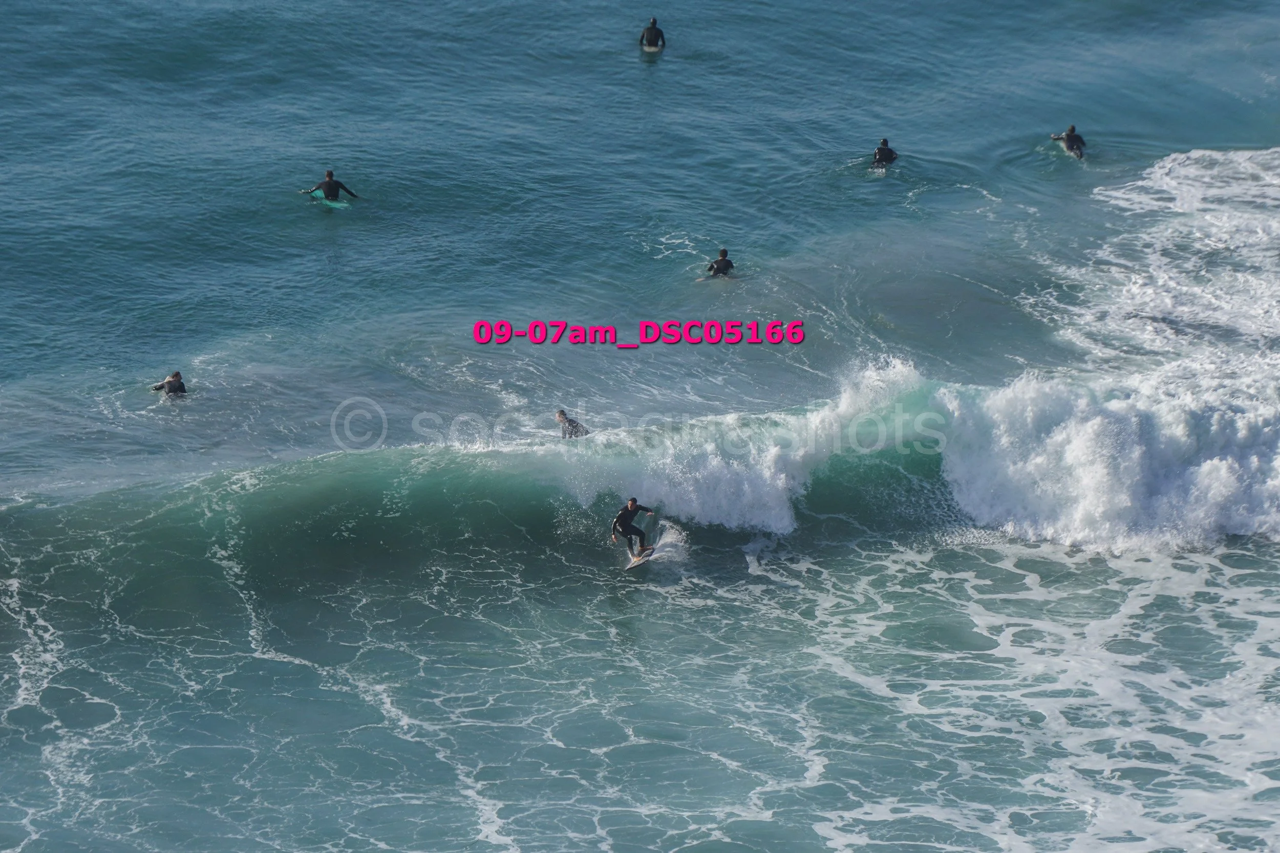 Group of surfers riding and waiting for waves in the ocean with some waves breaking in the foreground.