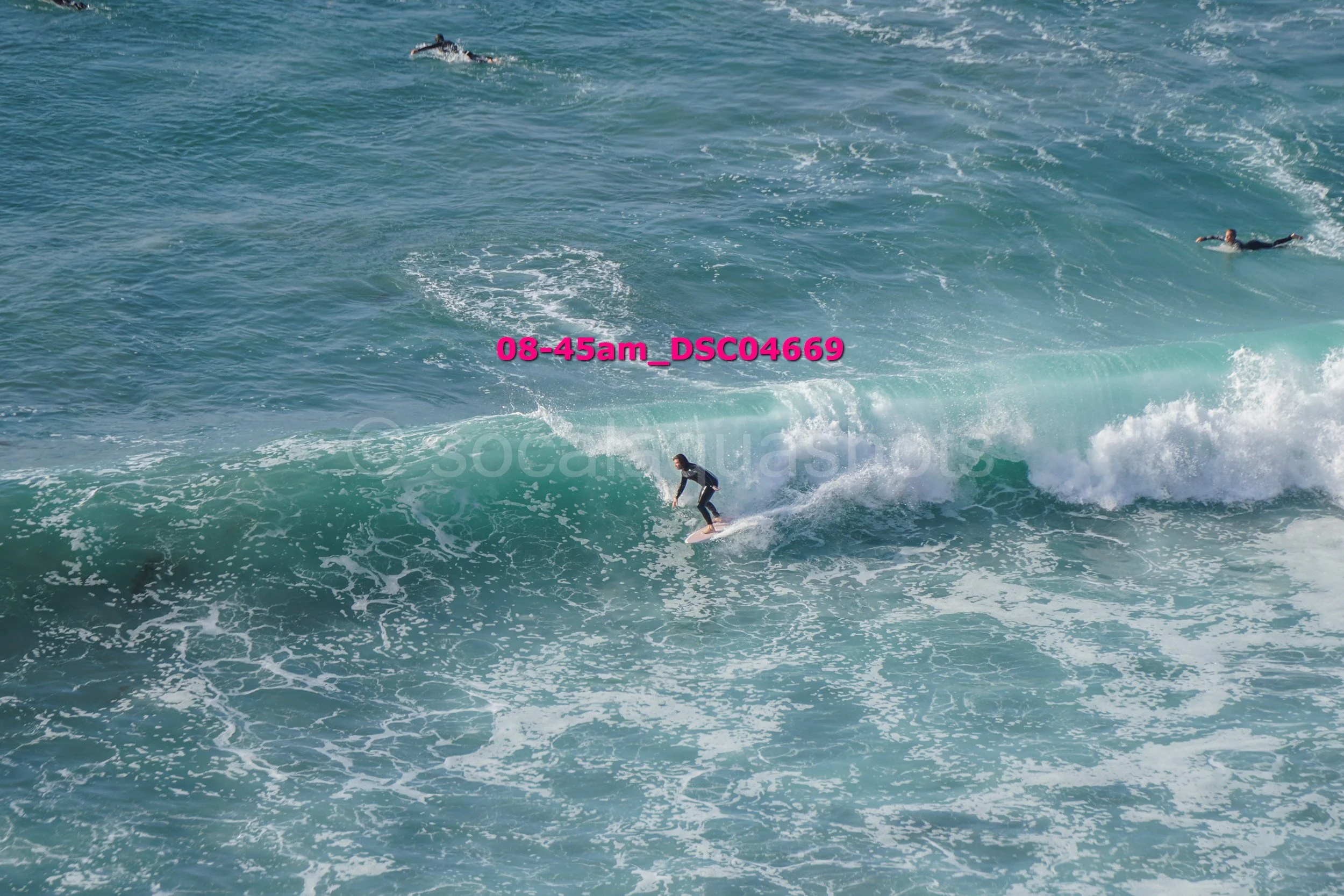 A person surfing on a wave in the ocean with two other surfers in the background.