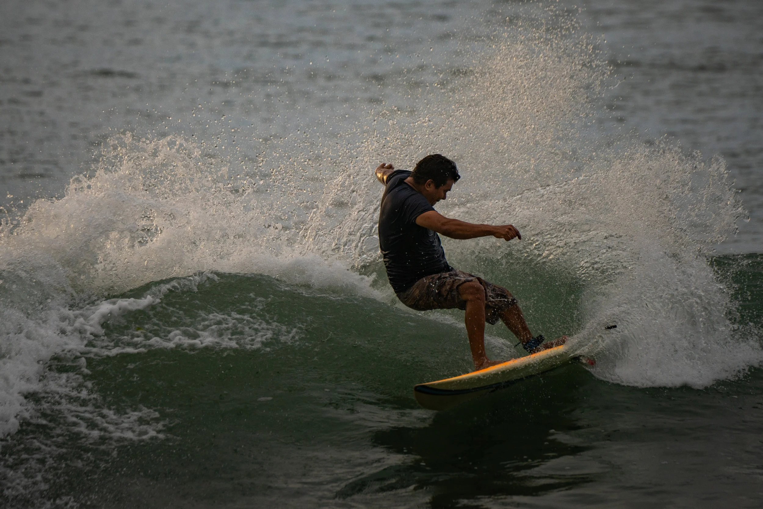 A man surfing on a wave in the ocean at sunset.