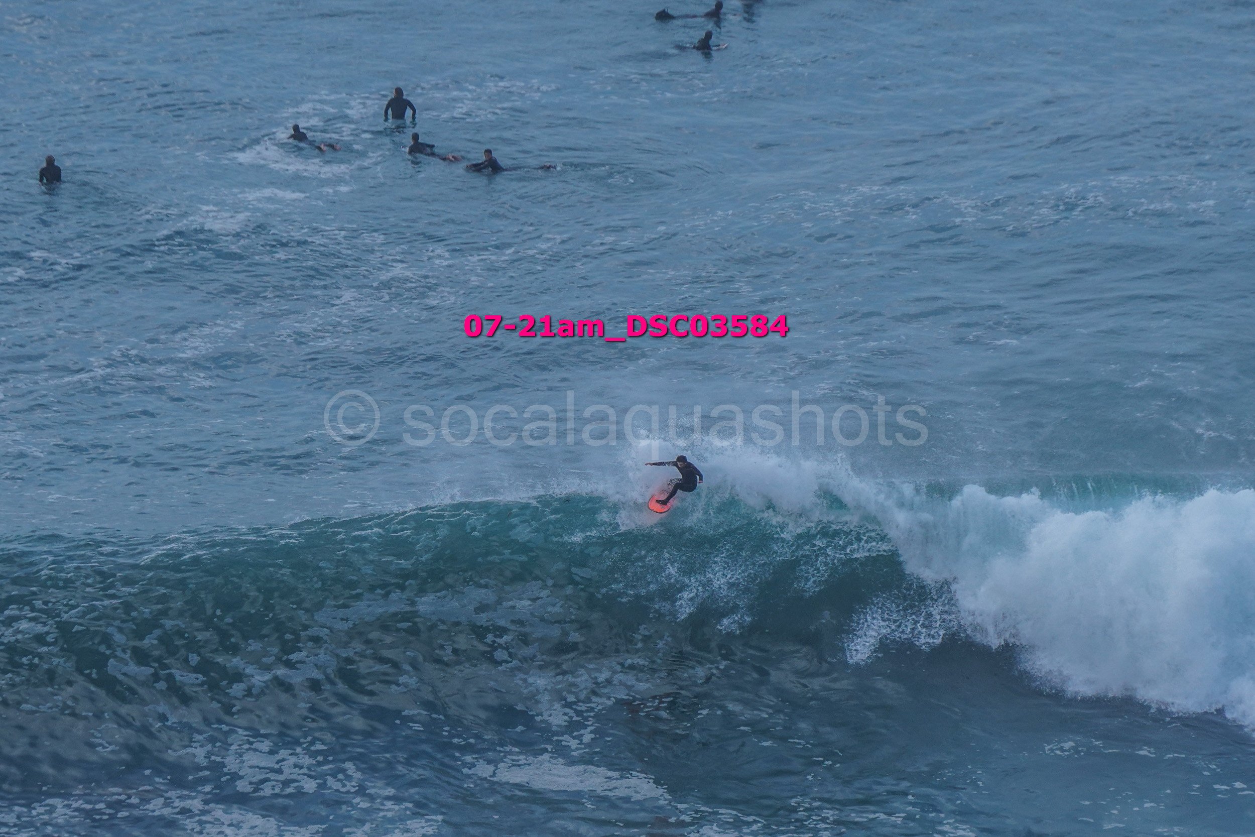 A person surfing on a wave with several swimmers in the water in the background.