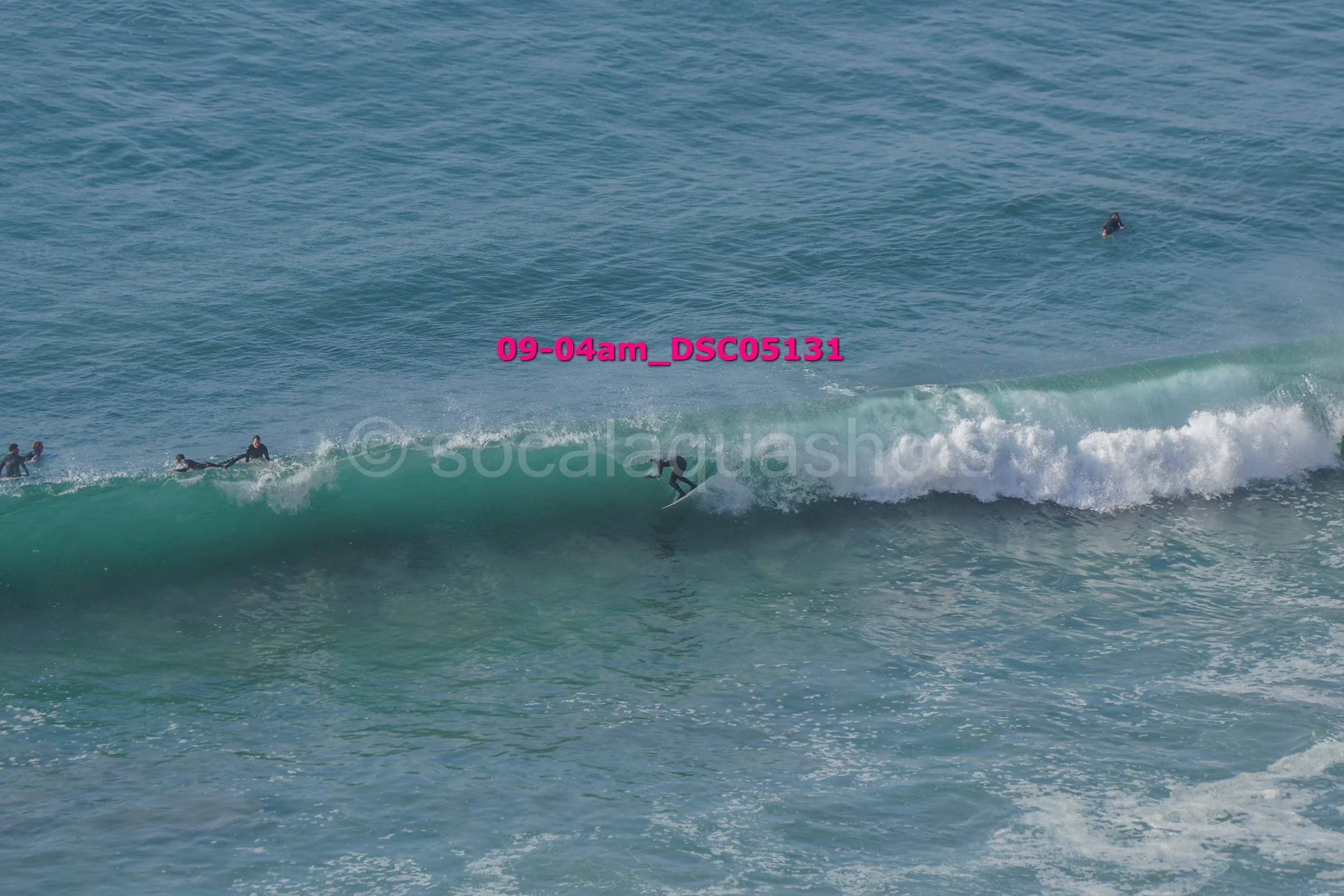 Surfer riding a wave near the shoreline with other surfers in the water.