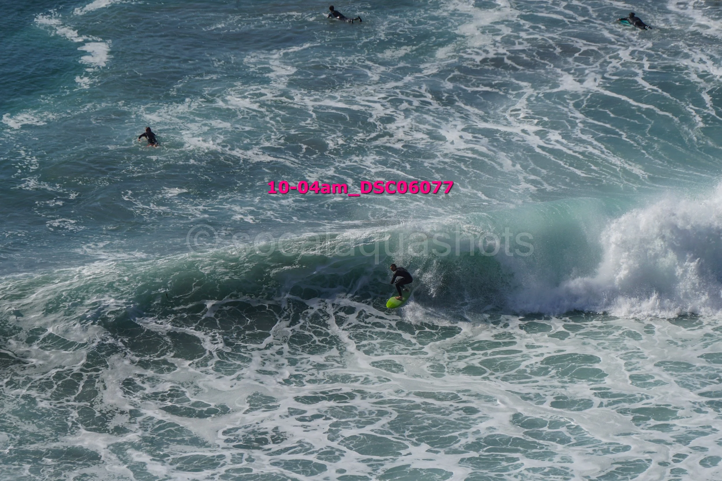 Surfer riding a wave in the ocean with two other surfers in the water nearby.