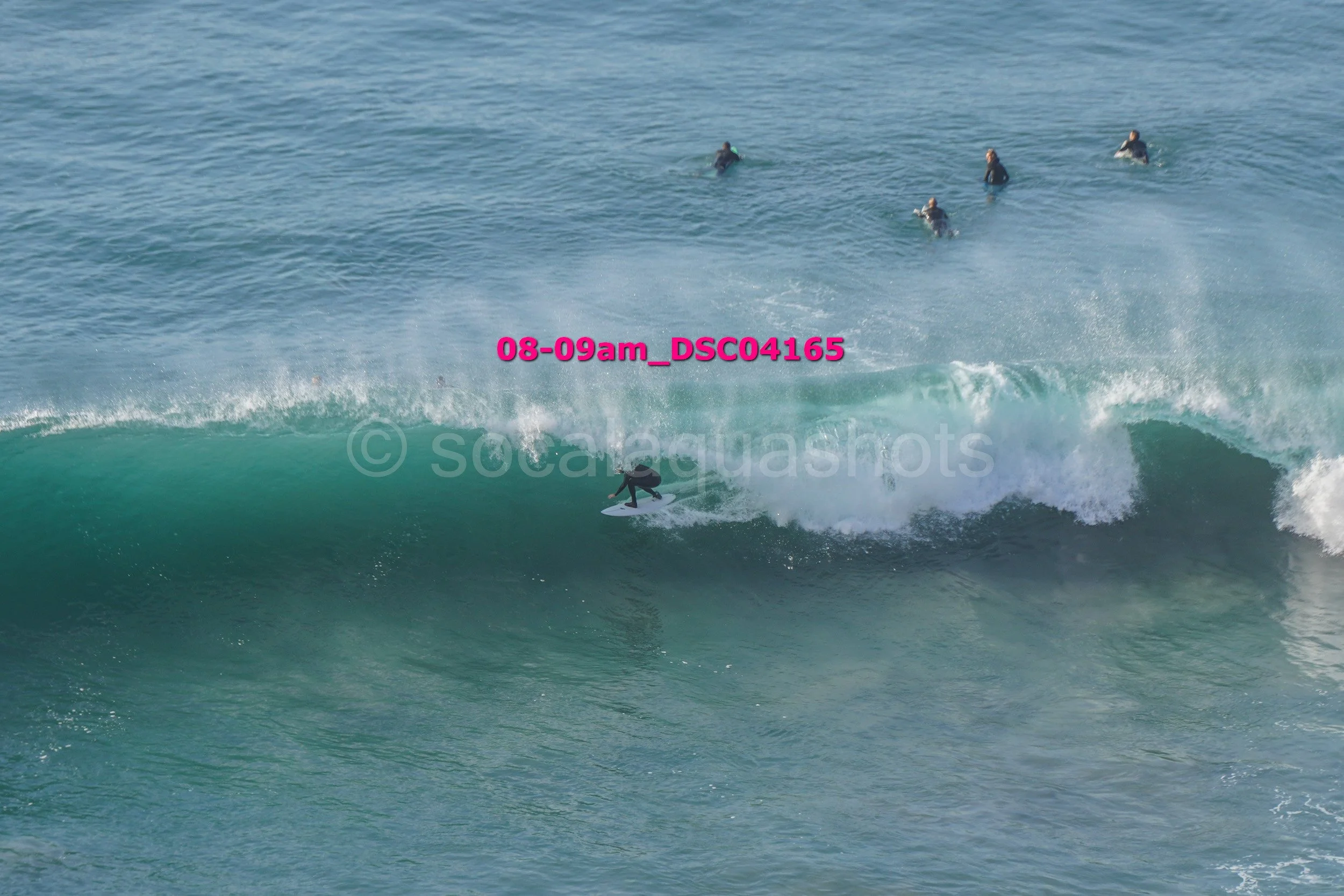 A person surfing on a wave with several other surfers in the background in the ocean.