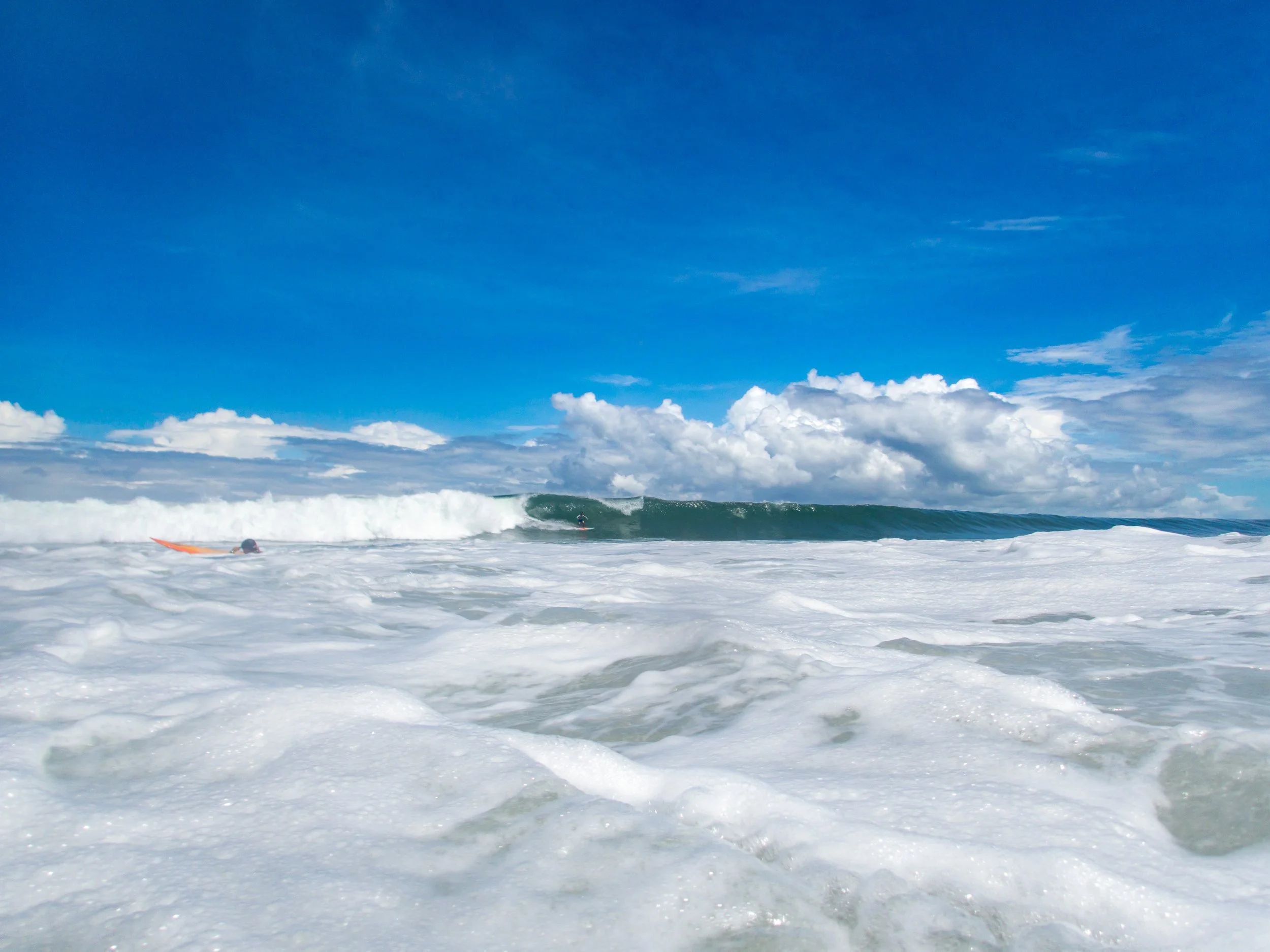Man surfs in ocean waves with cloudy blue sky background.