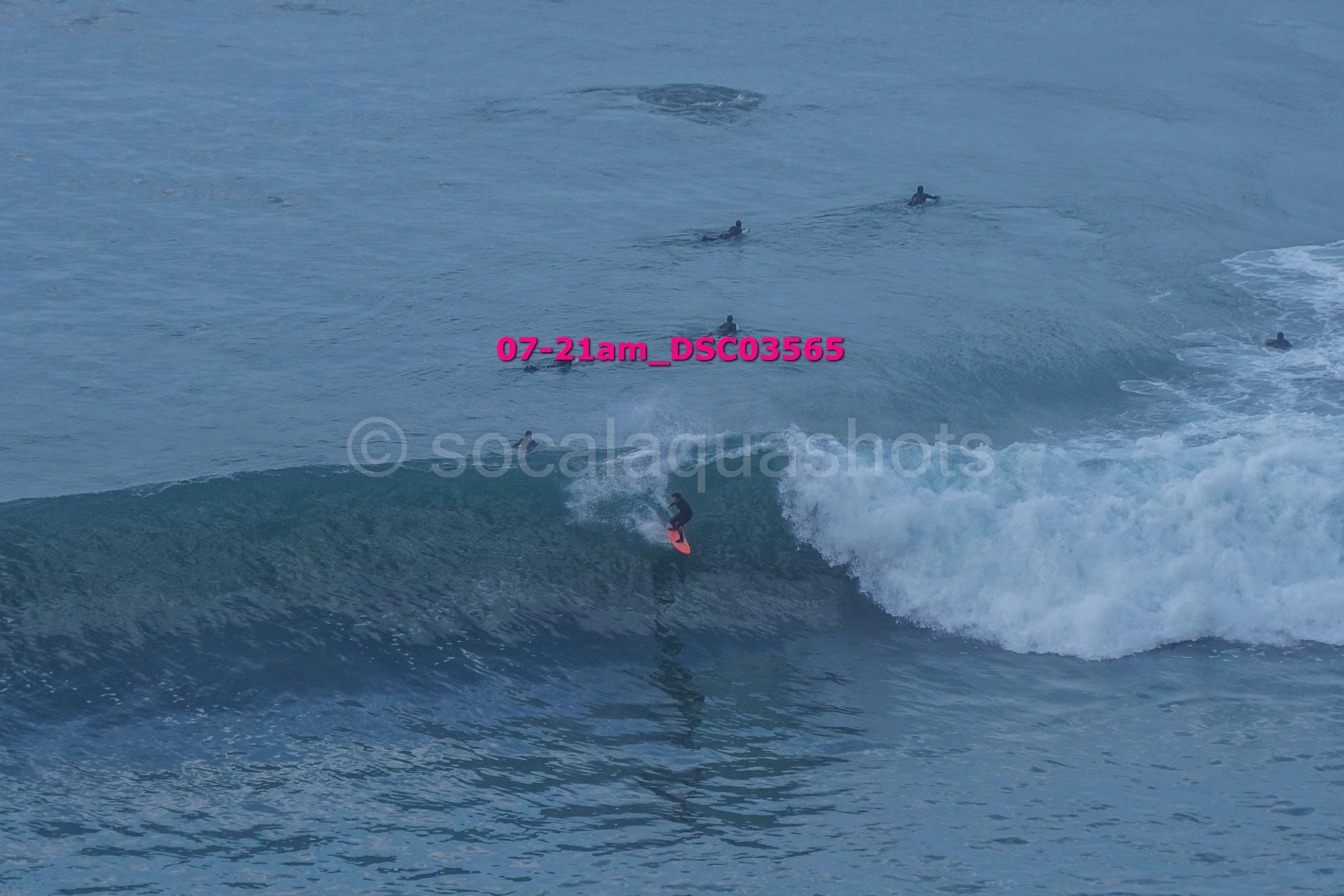A person surfing on a wave with several other surfers in the water nearby.