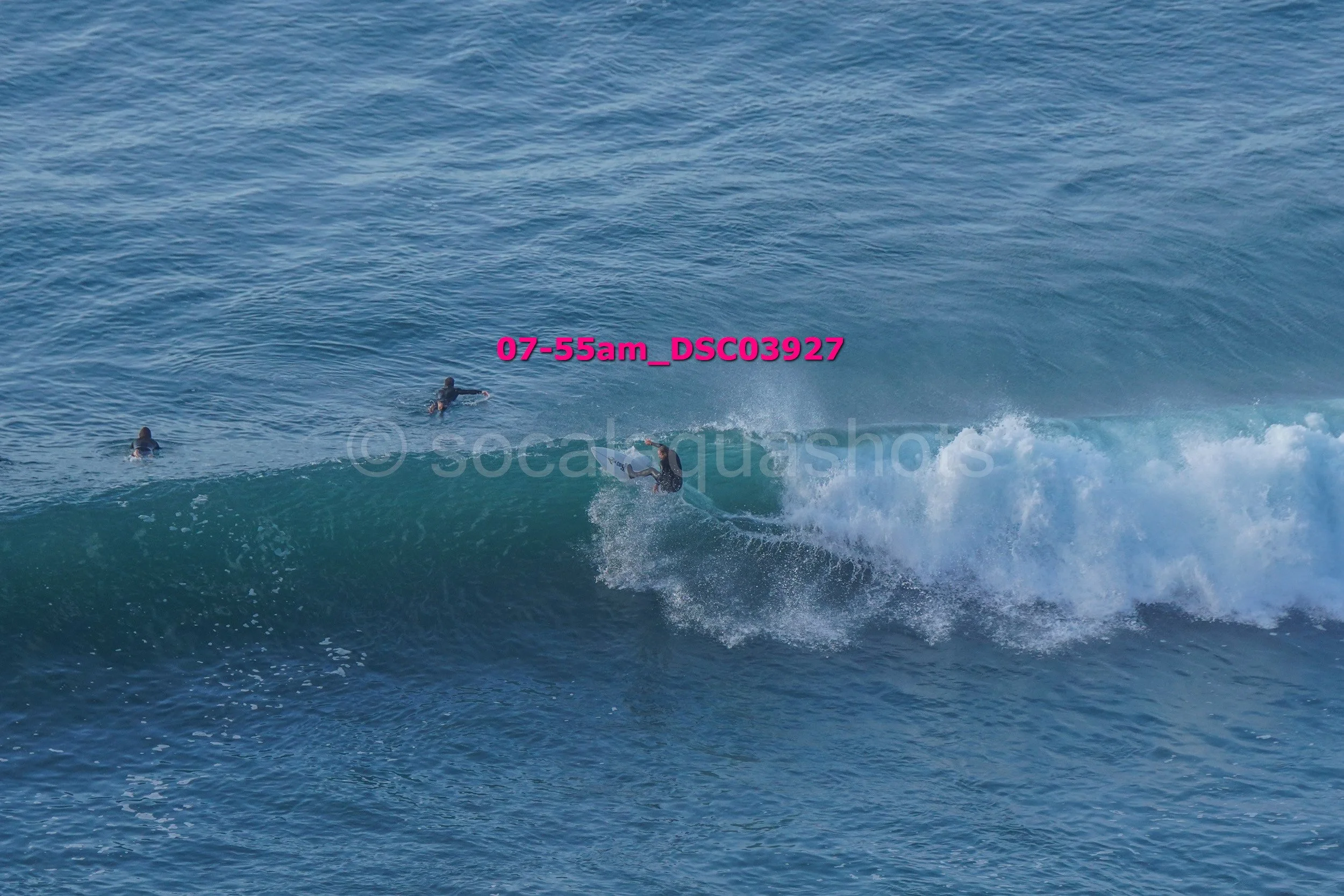 Surfer riding a wave with two other surfers paddling in the background in the ocean.