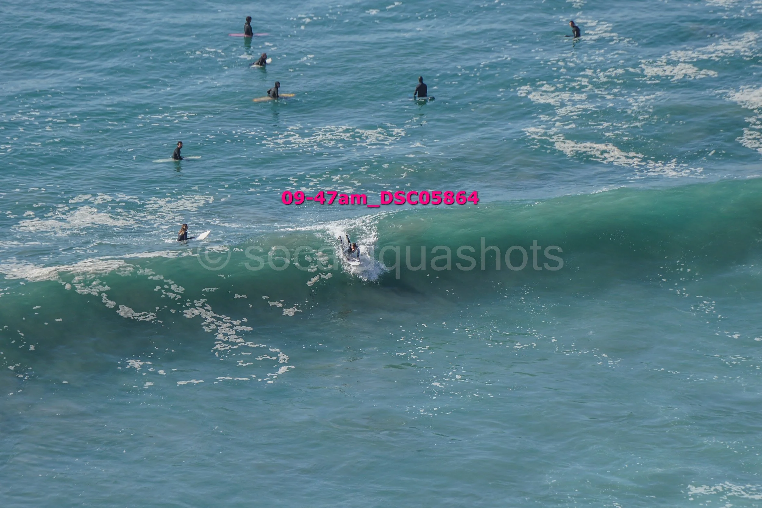 People surfing and swimming in the ocean with a visible wave and water splashes.