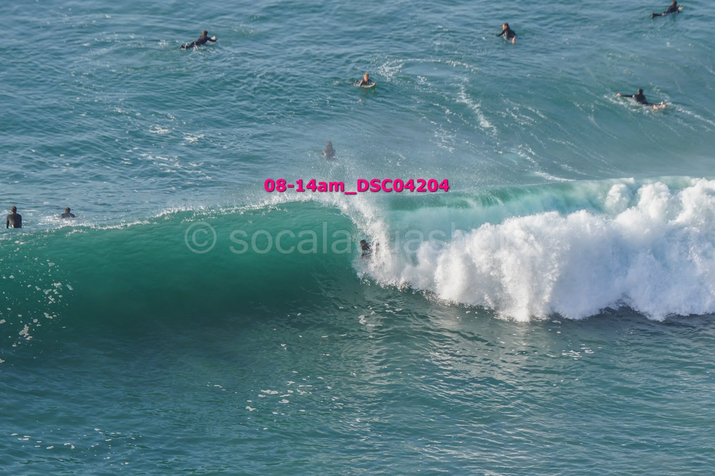 A person surfing on a large ocean wave with multiple surfers floating in the water nearby.