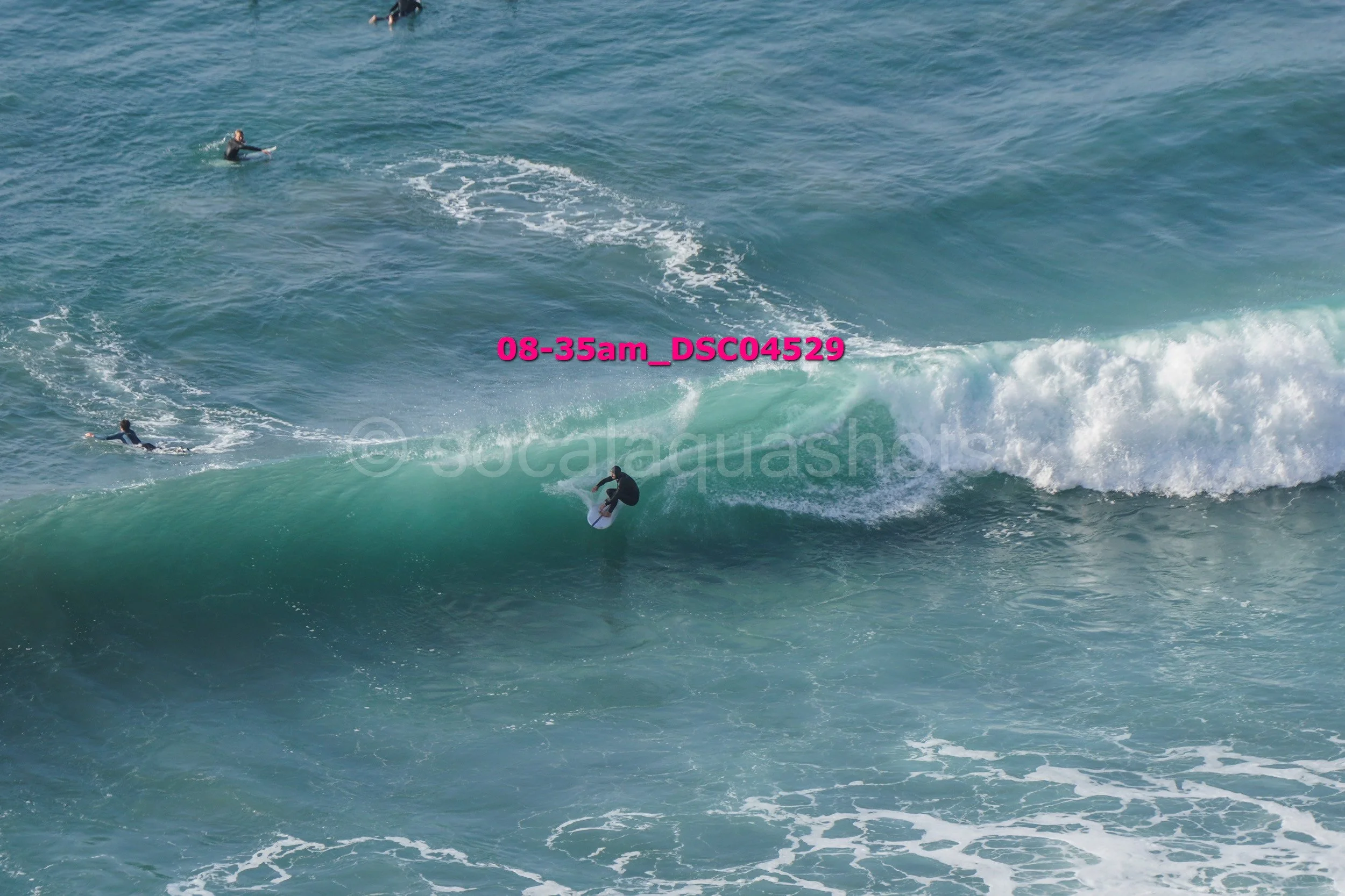 Surfer riding a wave with two other surfers in the background in ocean water.