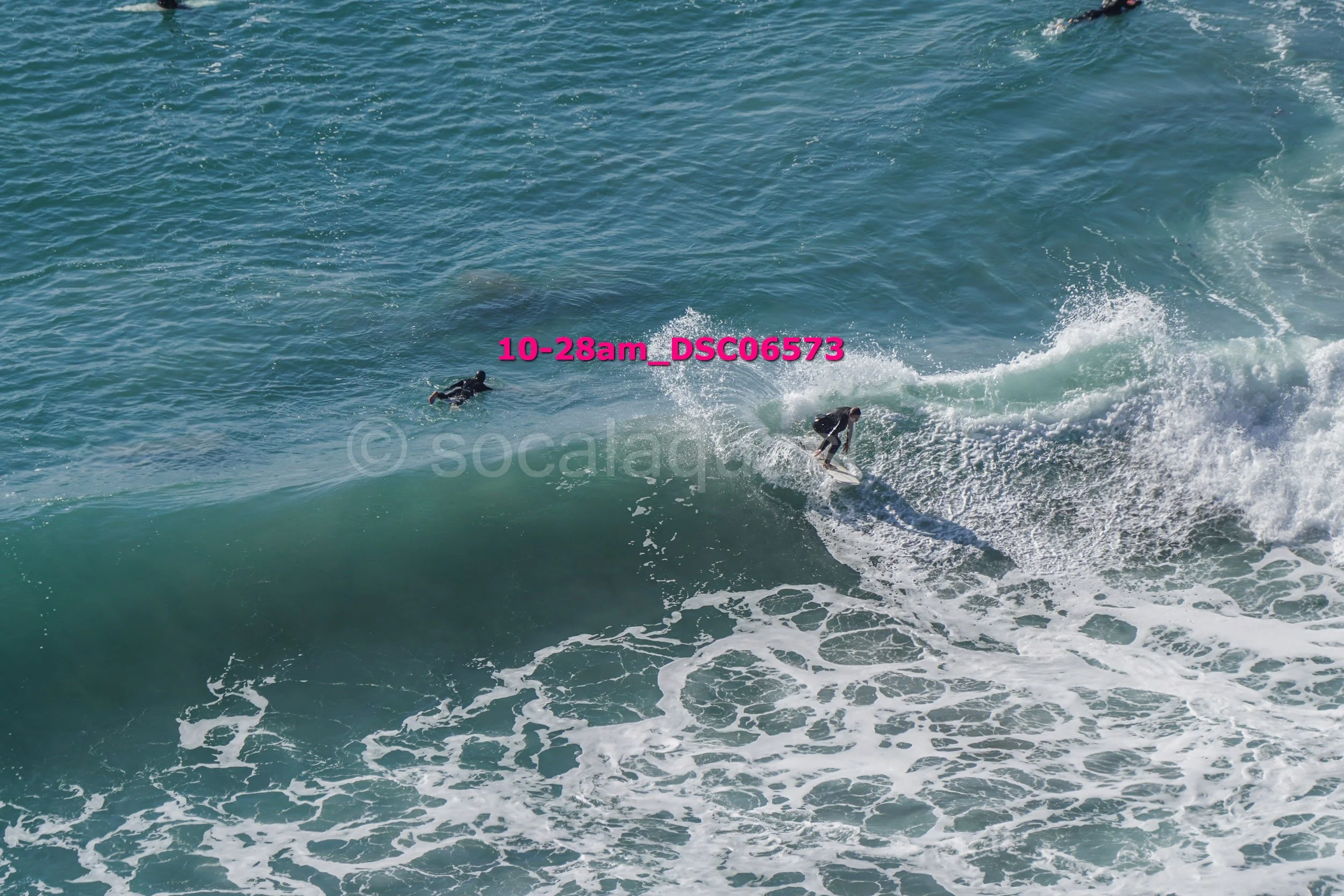 A person surfing on a wave in the ocean while another person swimming nearby.