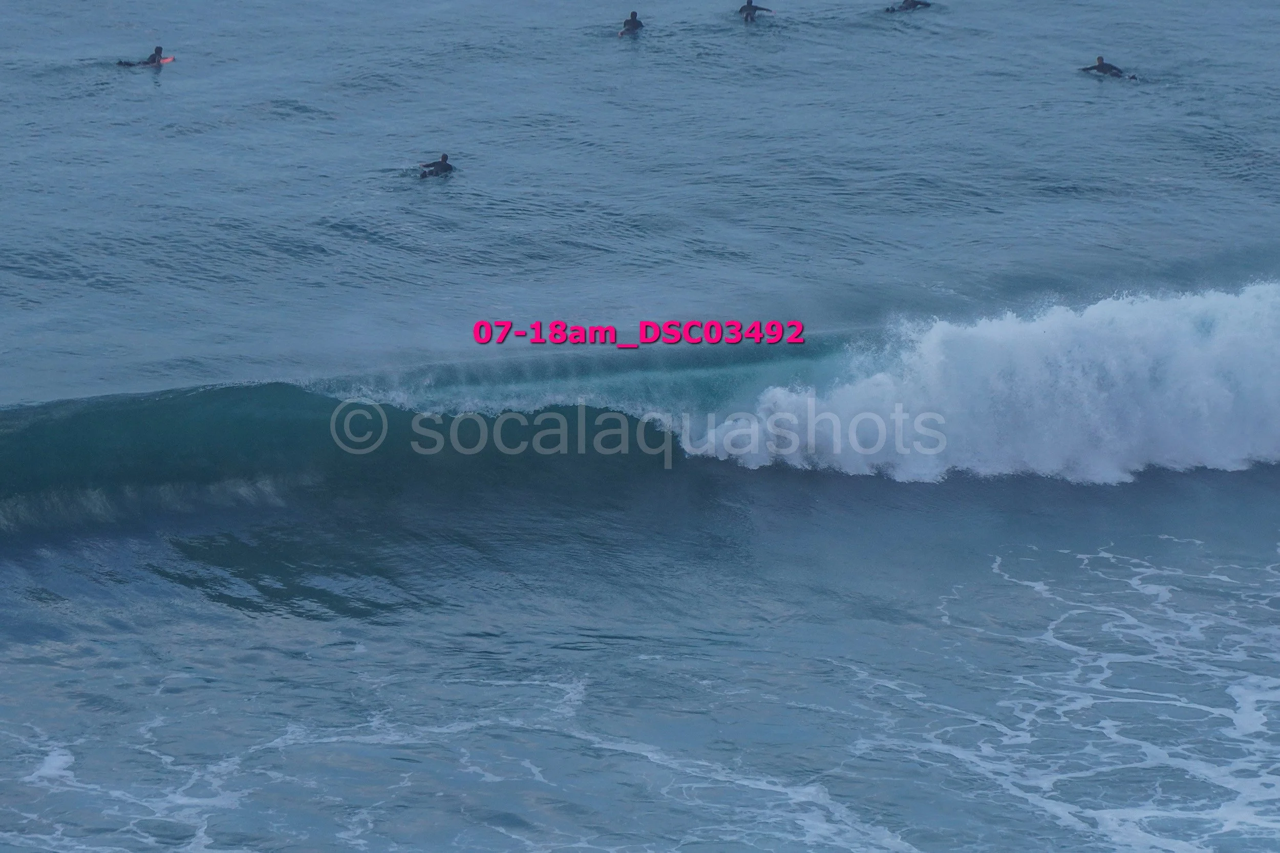 Several surfers in the ocean, with some sitting on their boards and others riding small waves.
