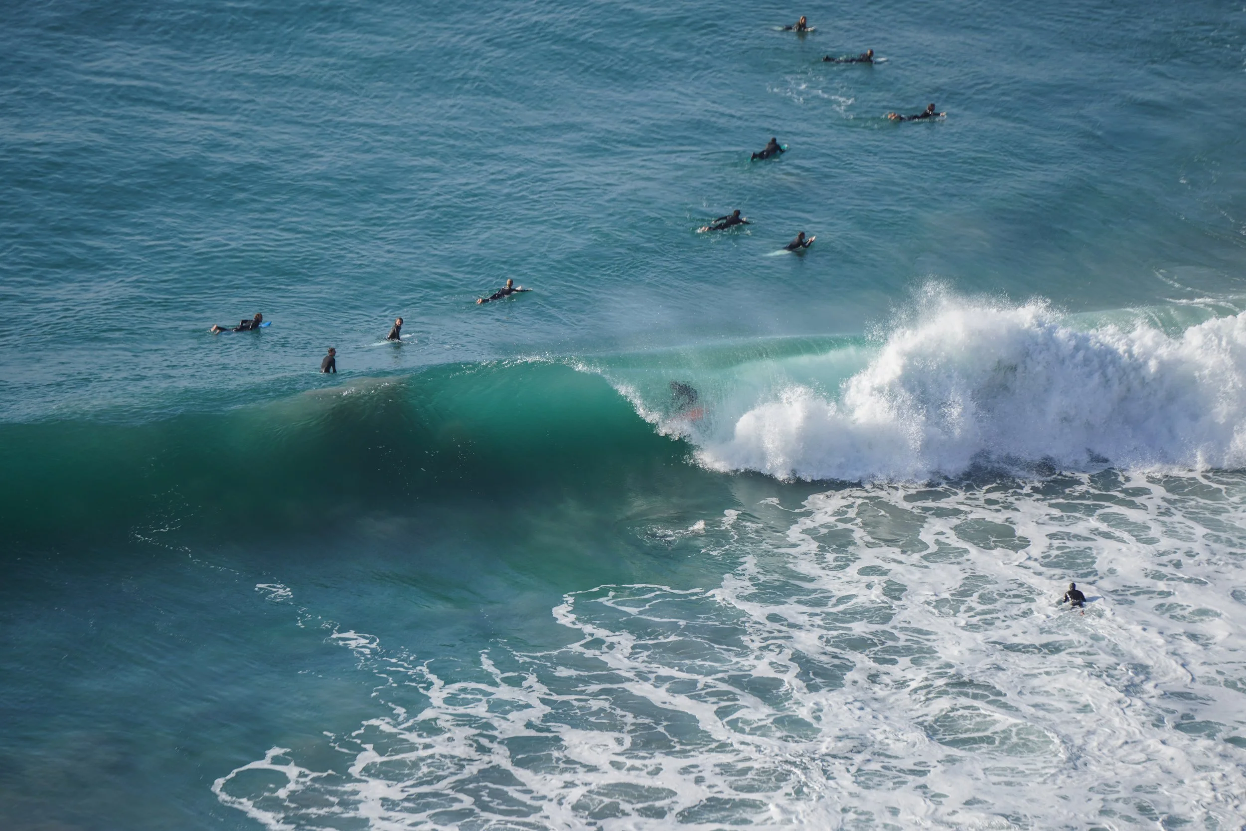 Multiple surfers in the ocean, some riding a wave and others waiting in the water.