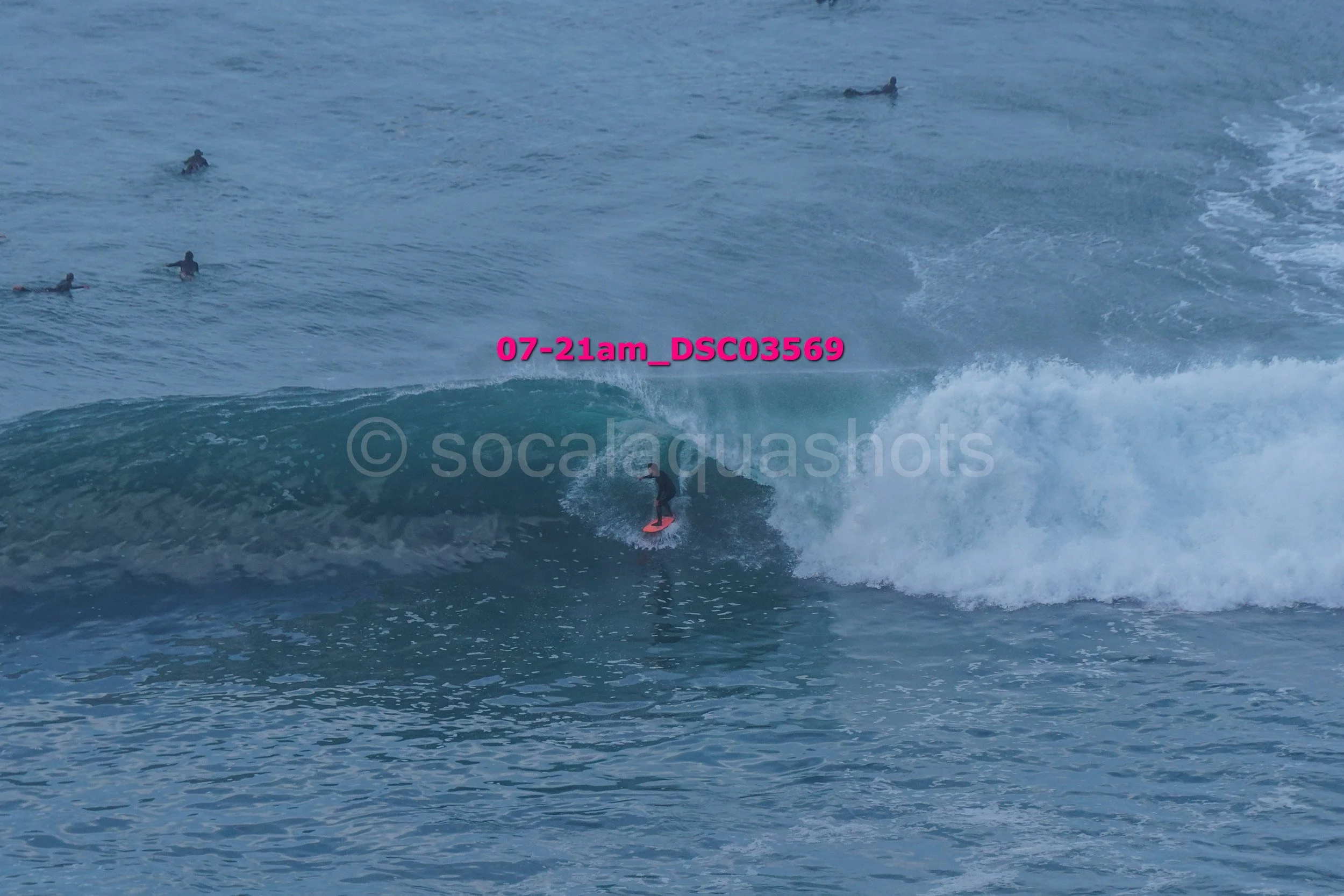 A person surfing a wave in the ocean, with several other people swimming in the background.