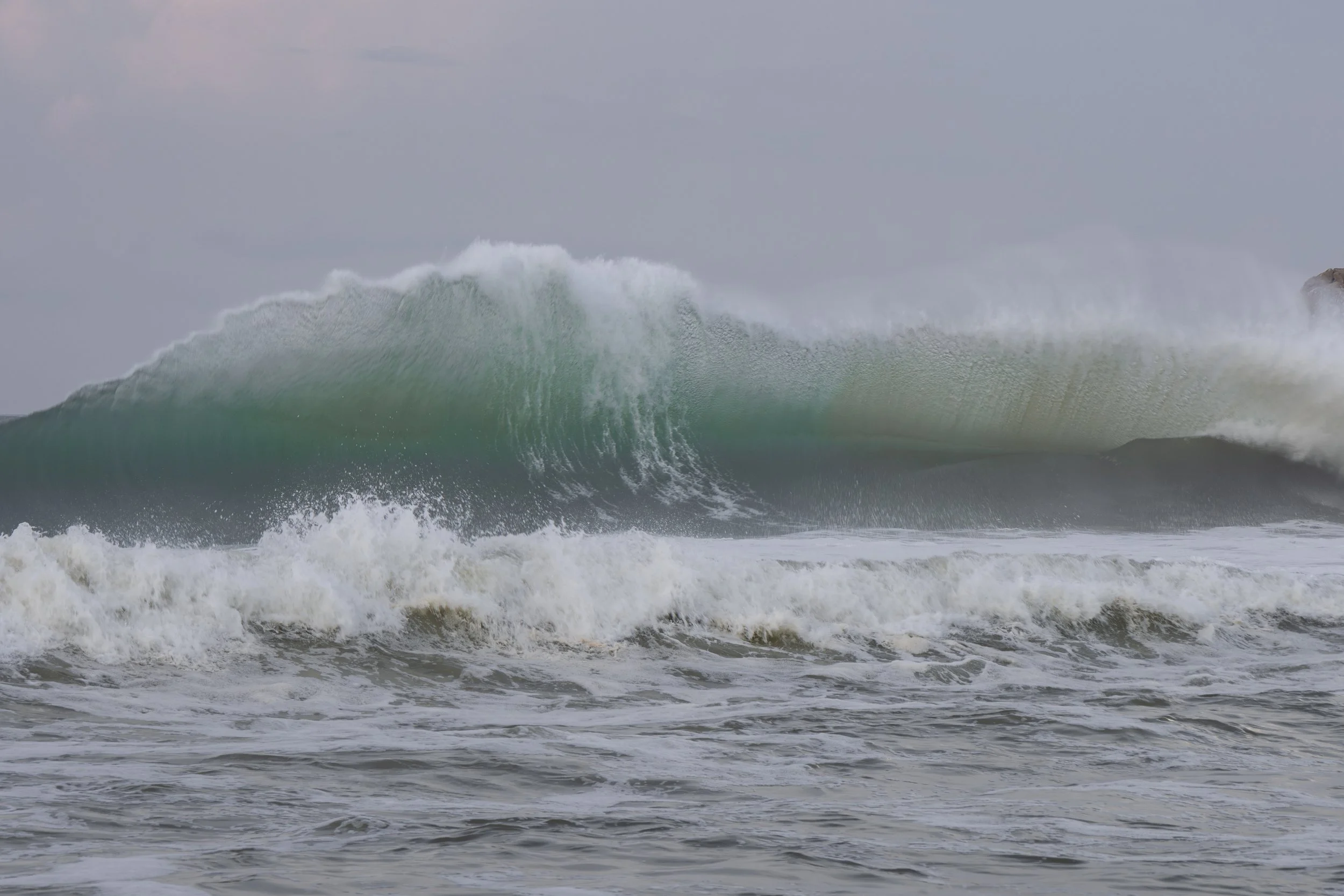 A large ocean wave crashing towards the shore with white foam and spray.