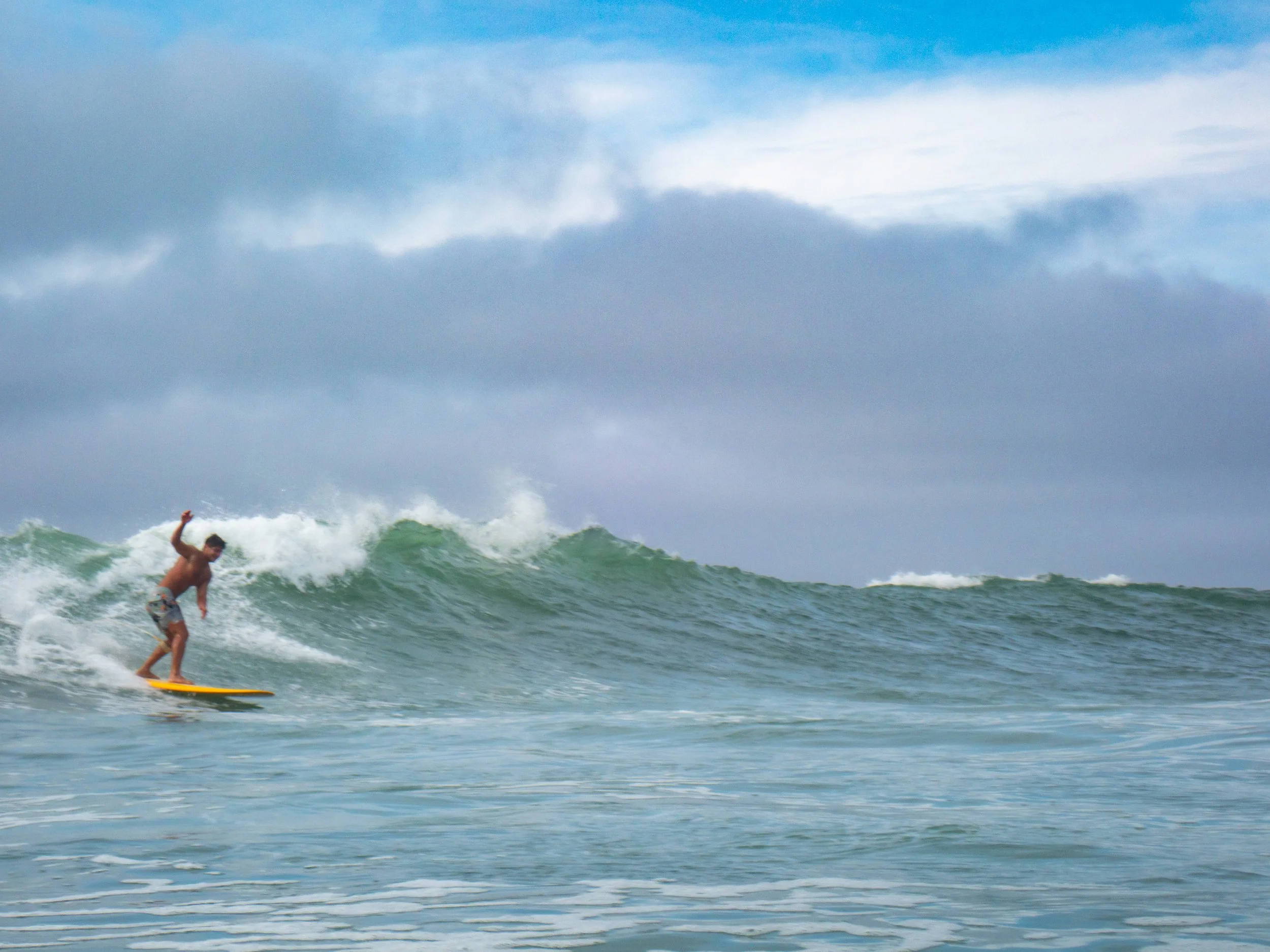 A man surfing on a wave in the ocean with a cloudy sky above.