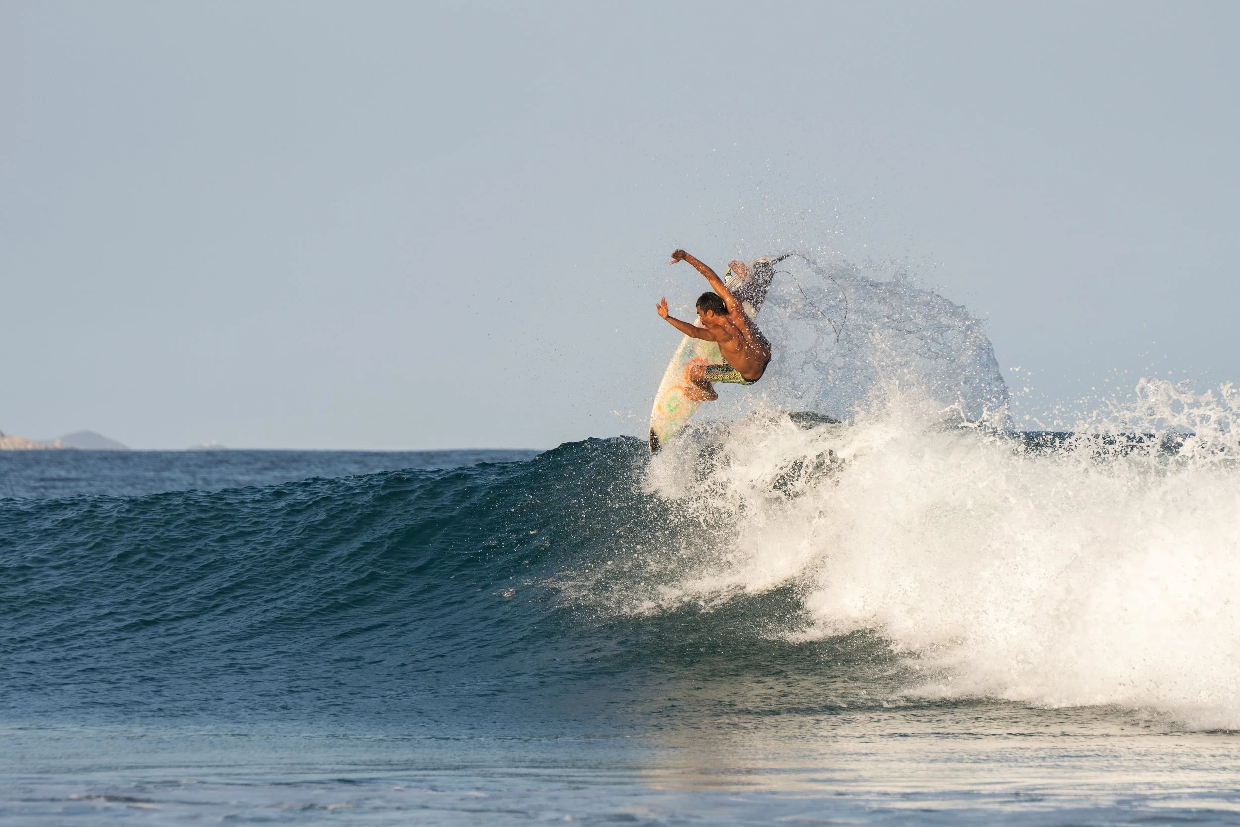 A person surfing on a wave in the ocean, with a clear sky in the background.