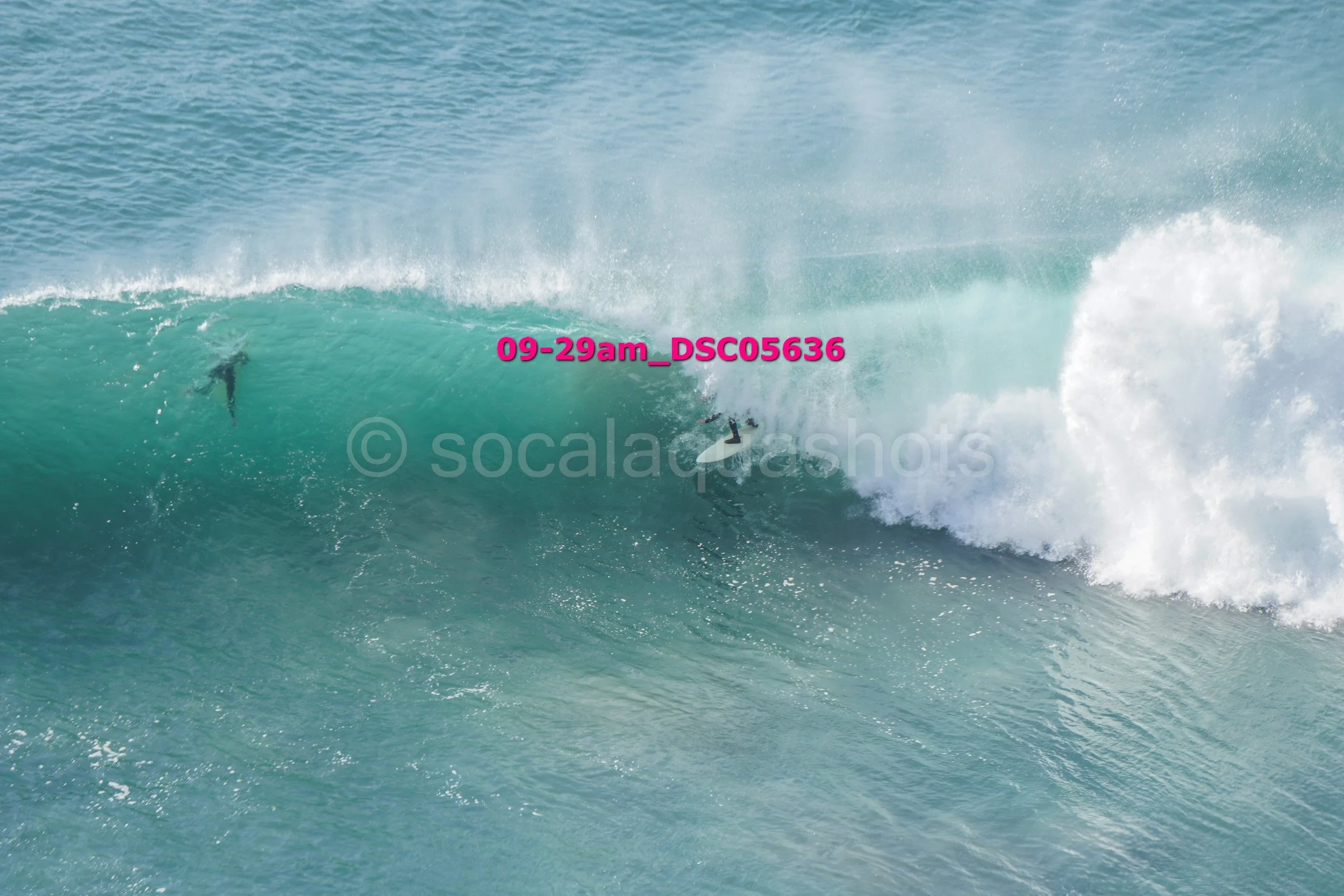 A surfer riding inside a large, turquoise wave with another surfer visible near the crest.