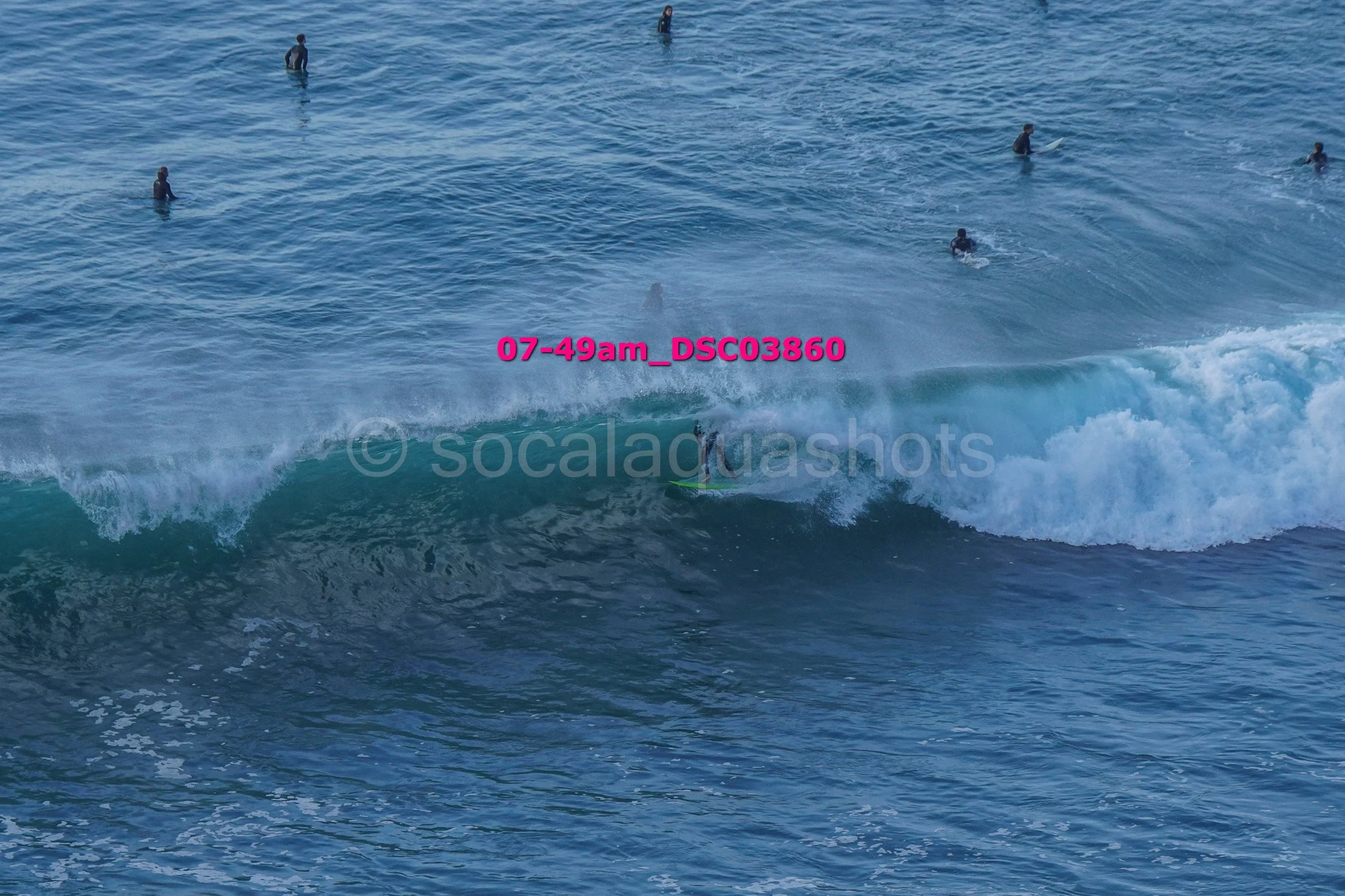 Surfer riding a wave in the ocean with several people in the water in the background.