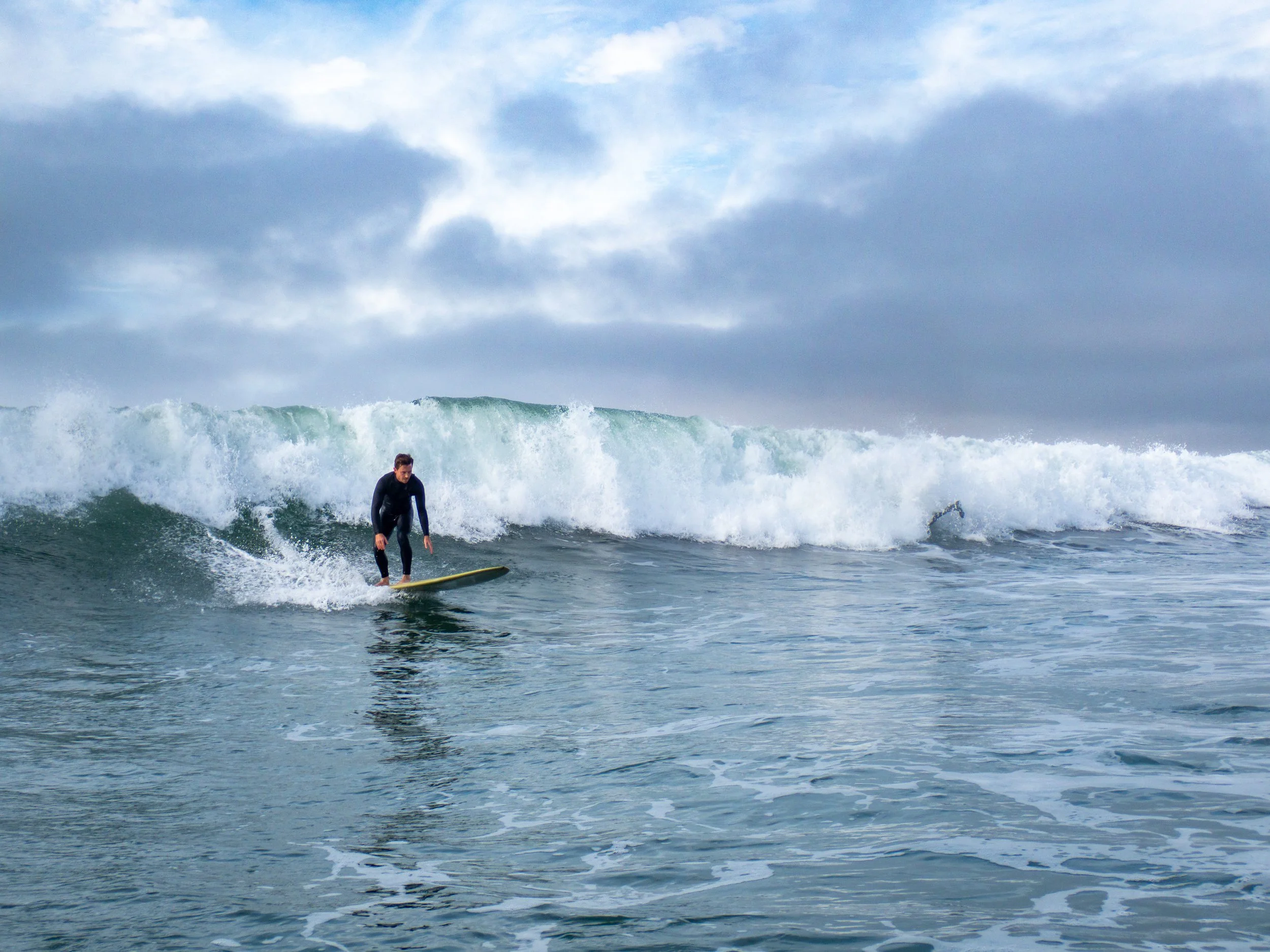 A person surfing on a wave in the ocean during cloudy weather.