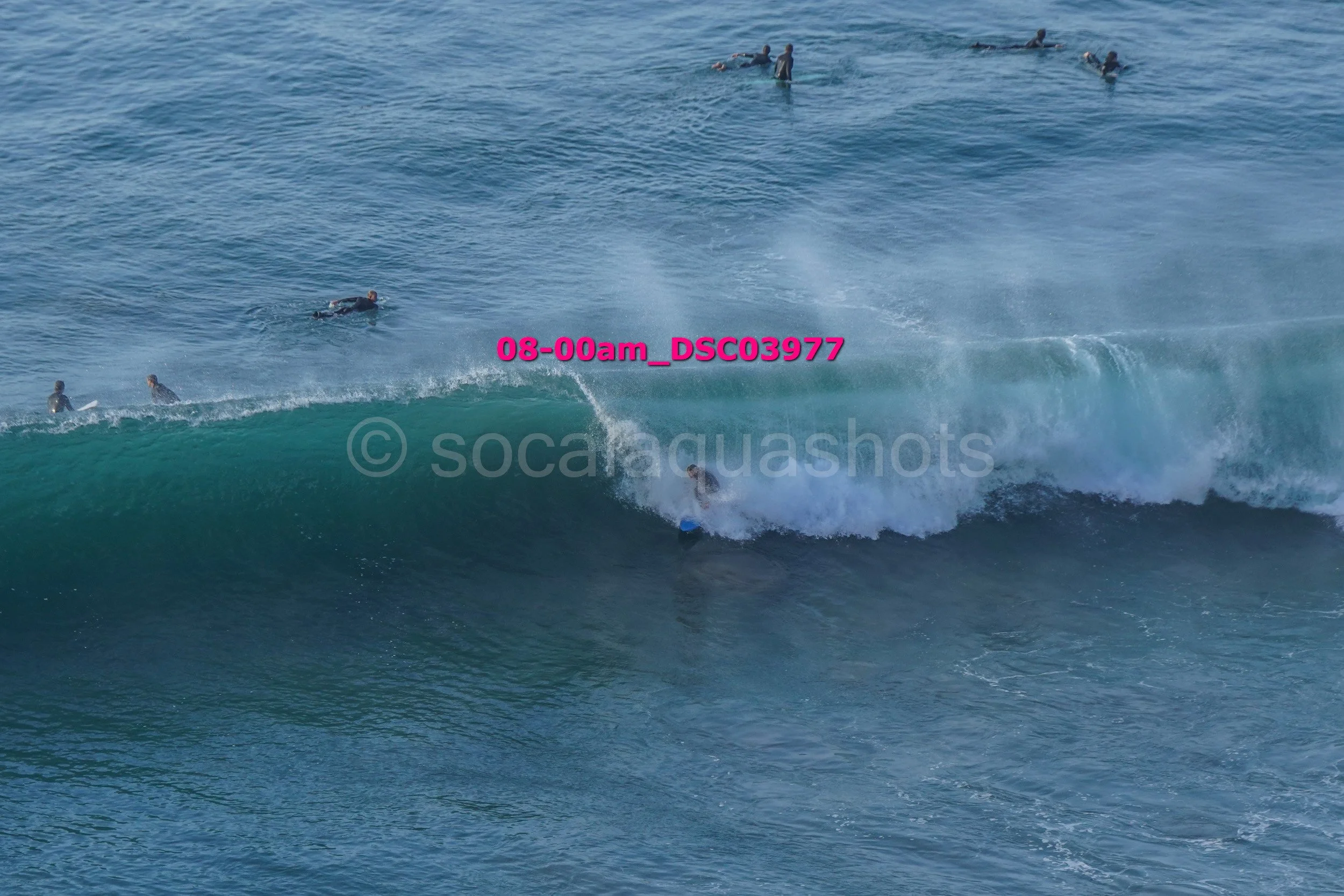 Surfer riding a large wave with several surfers in the water in the background.