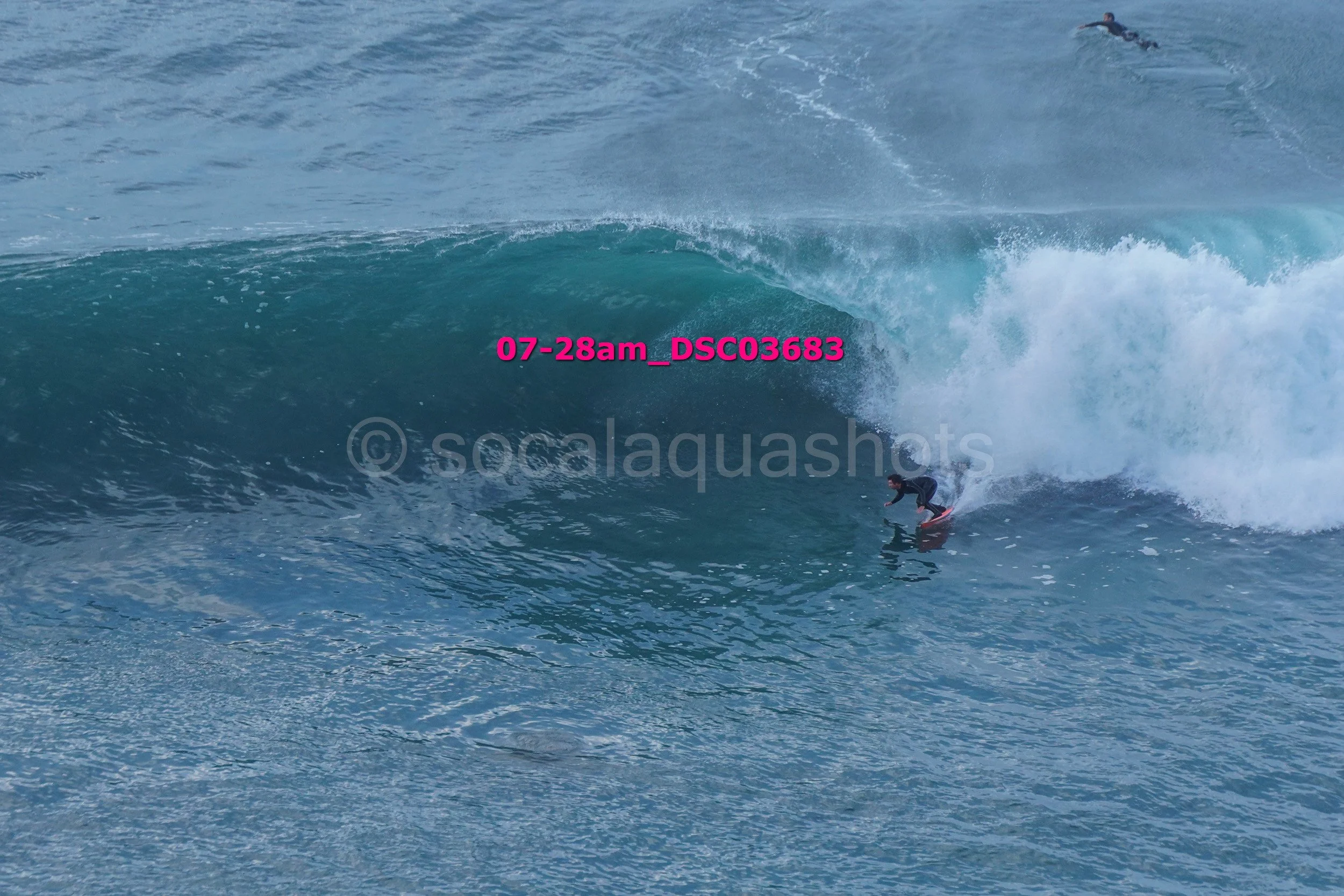 A person surfing on a breaking ocean wave with another surfer in the background.