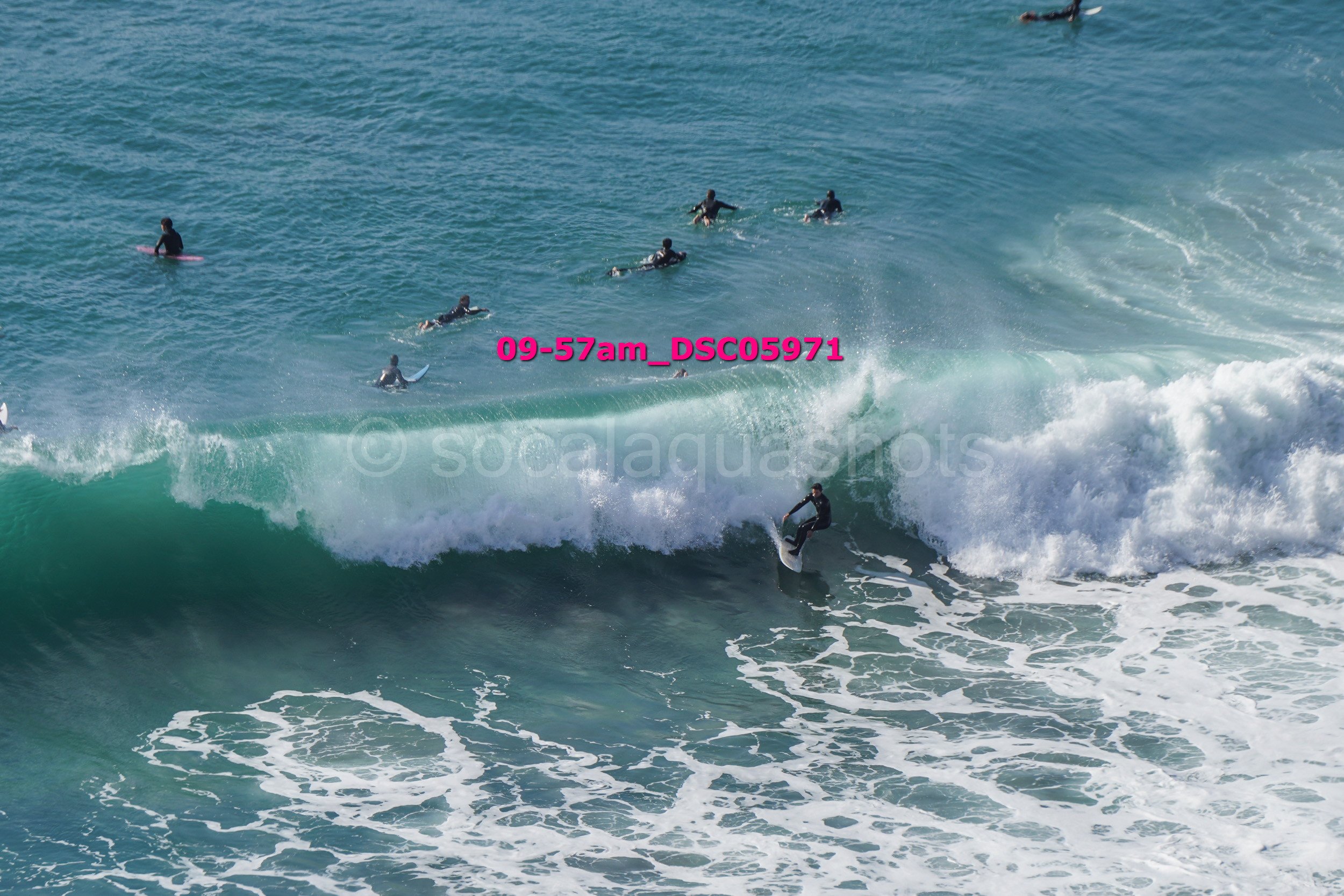 Surfer riding a wave with multiple surfers in the water behind him.