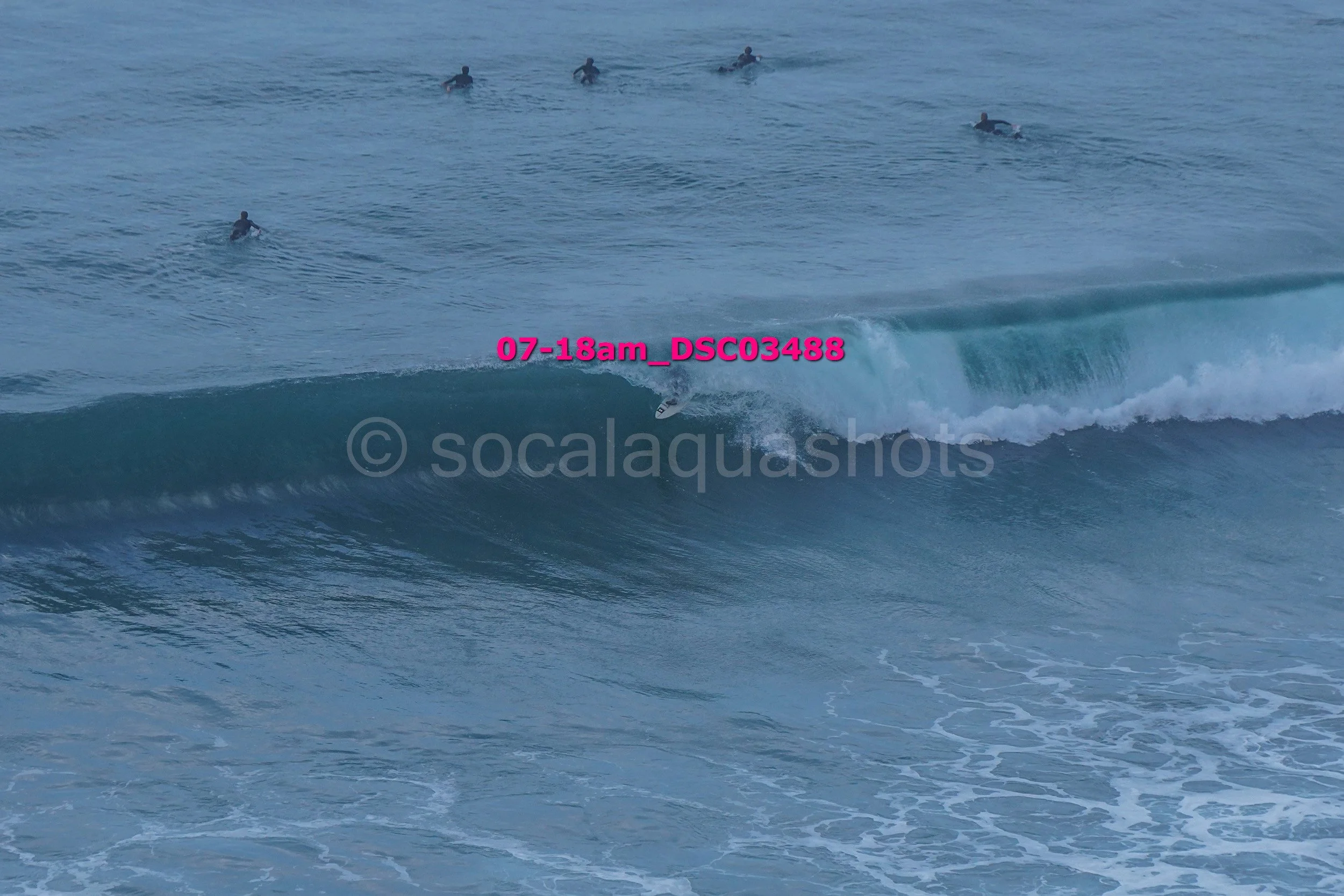 A surfer riding a wave with several other surfers in the water nearby.