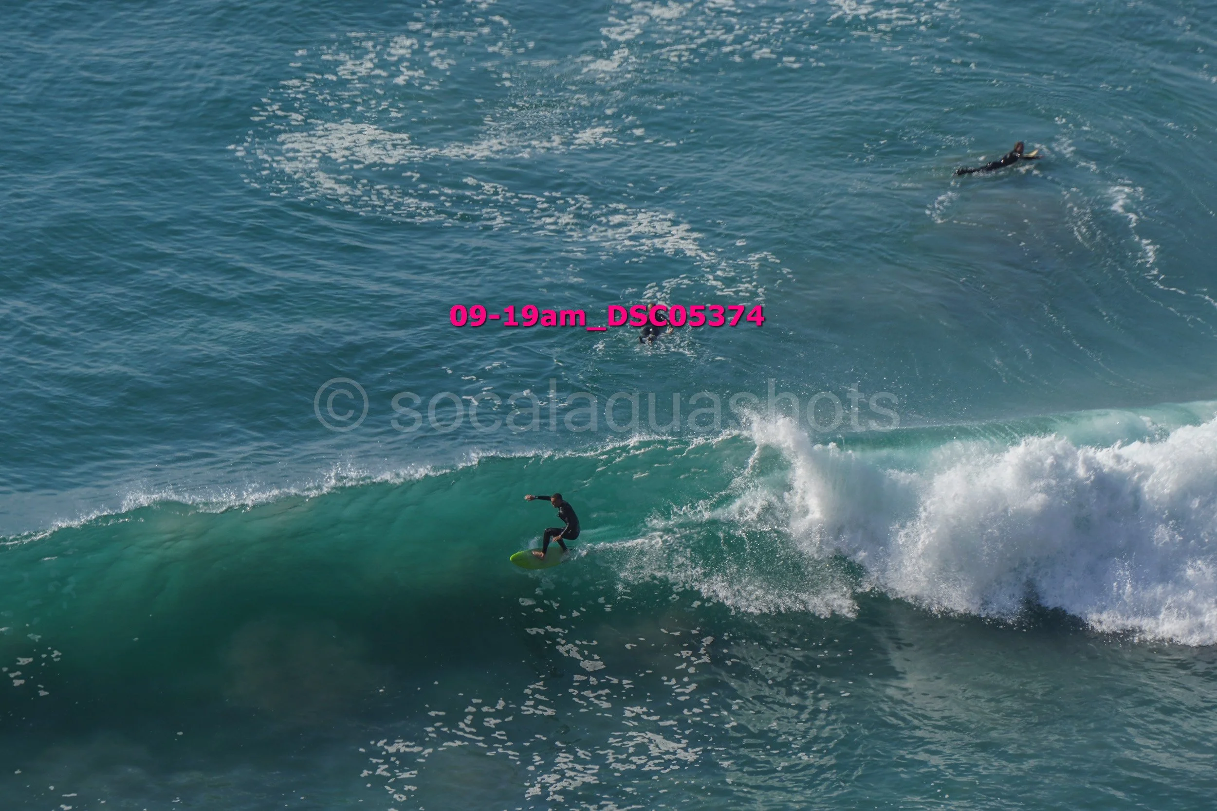 A surfer riding a wave with two surfers swimming in the water nearby.