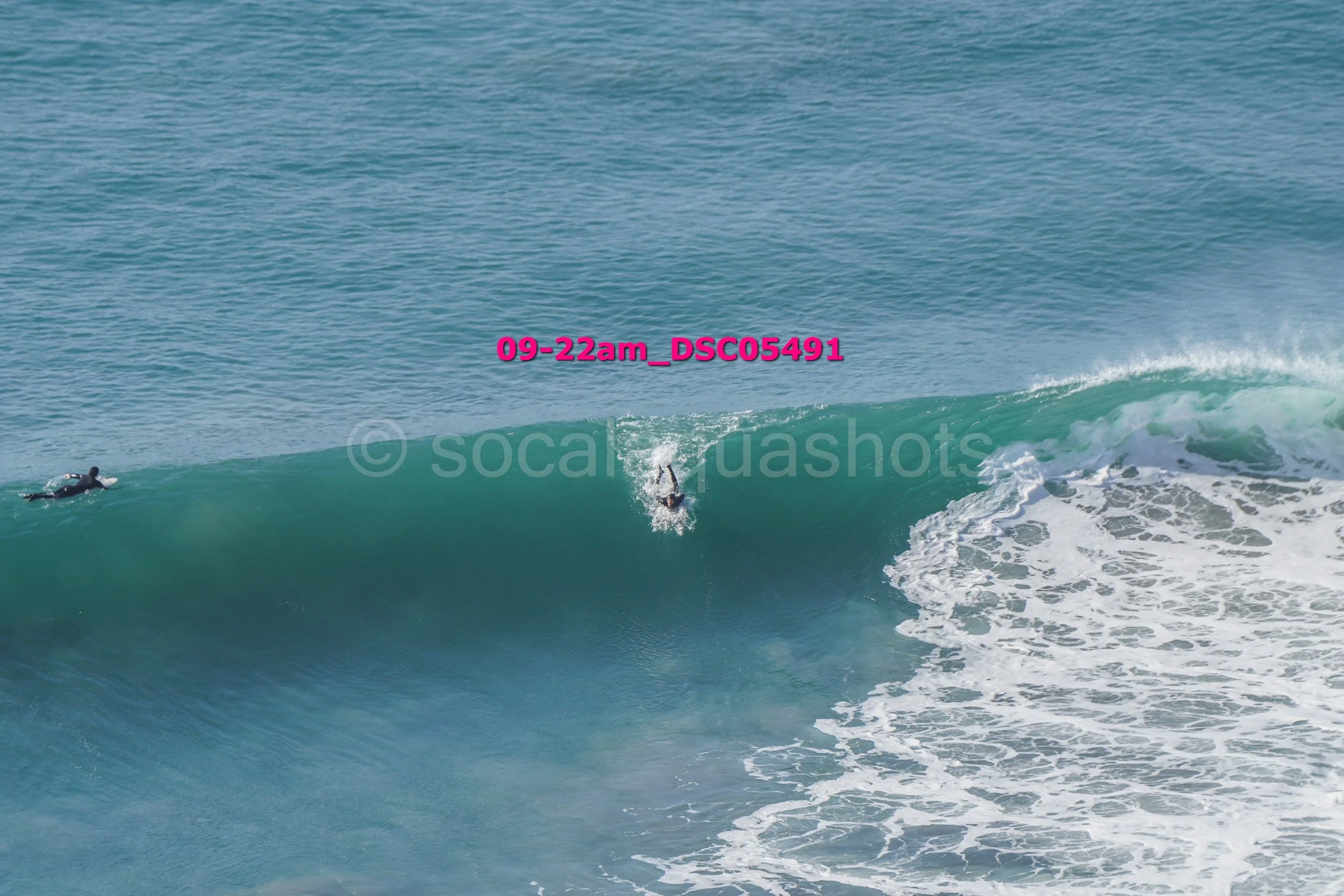 A person surfing on a wave in the ocean, with another person lying on a surfboard nearby.