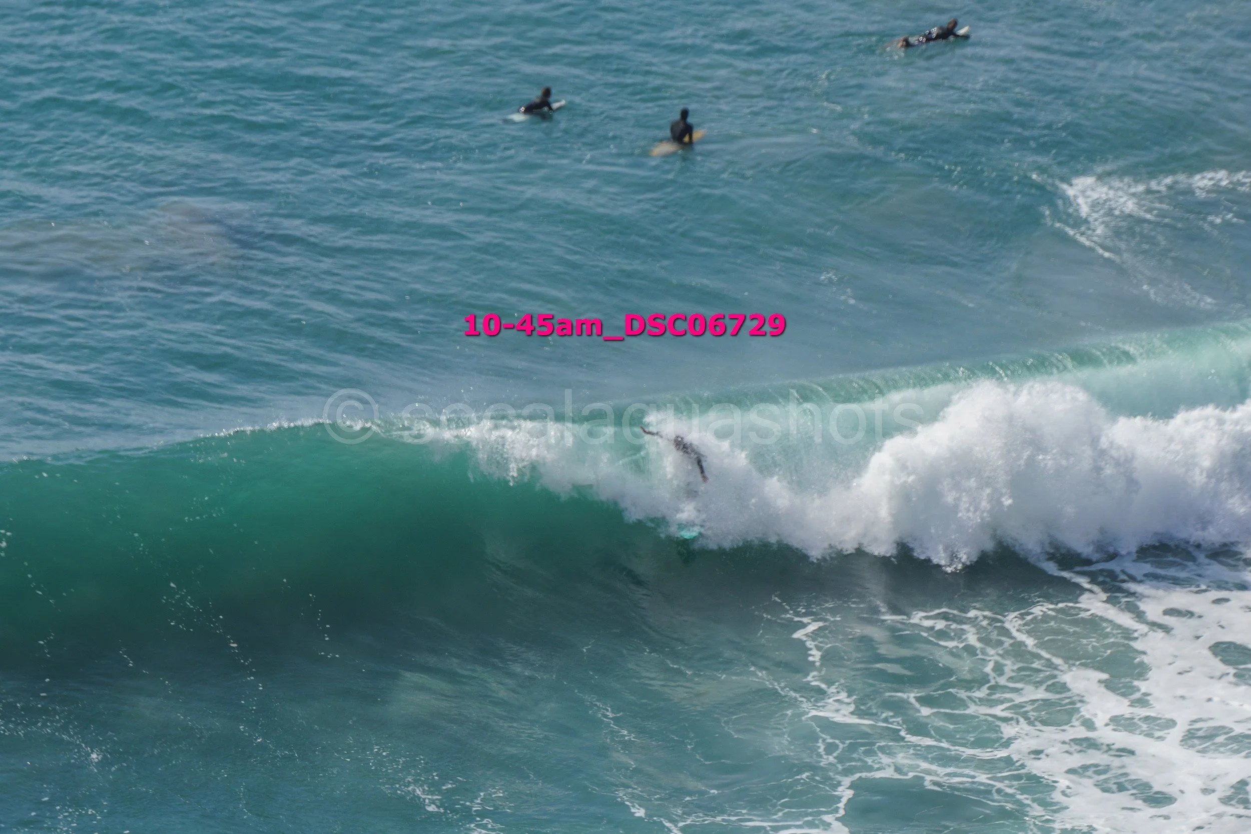 Surfer falling off surfboard while riding a wave in the ocean with three surfers in the background.