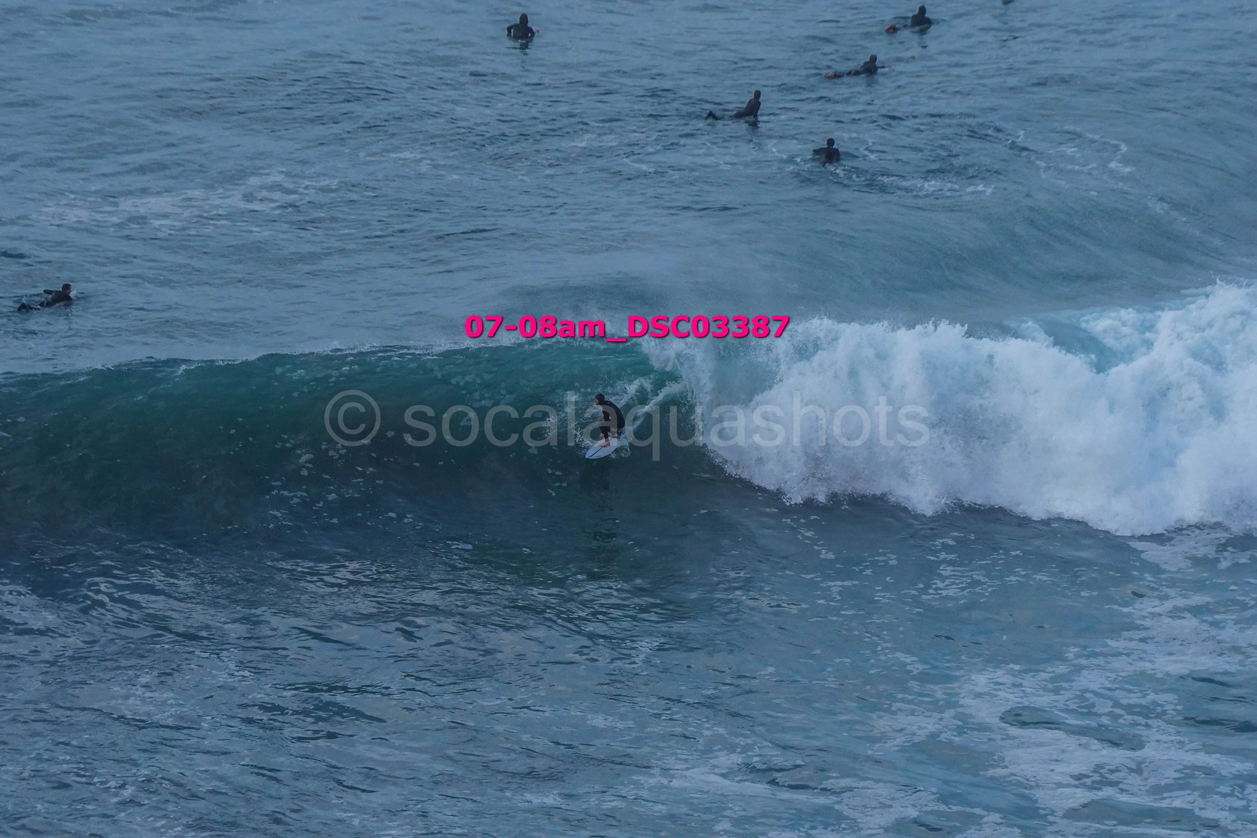 A person surfing on a wave with multiple surfers in the water in the background.