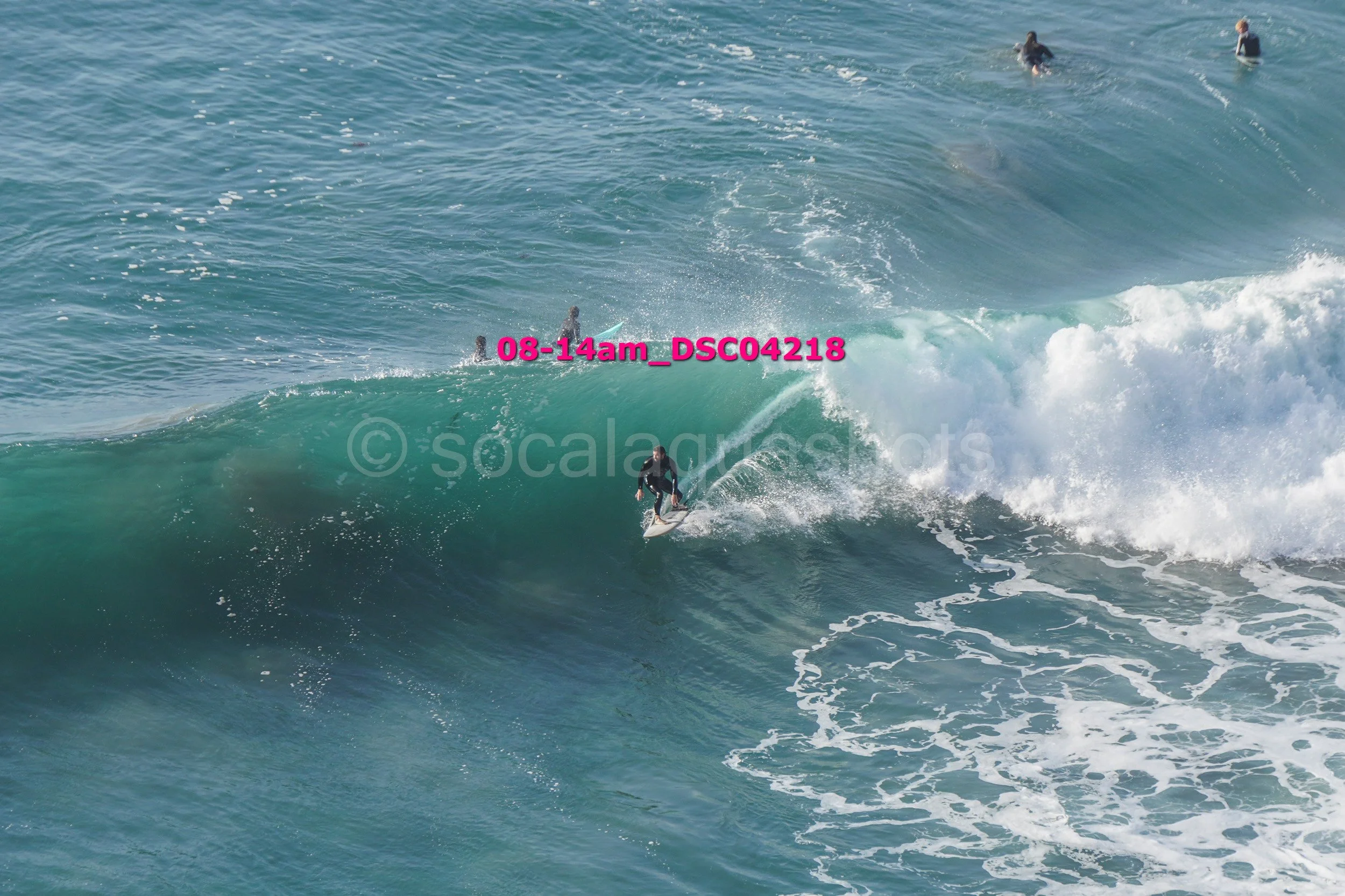 Surfer riding a large wave with several people in the water in the background.